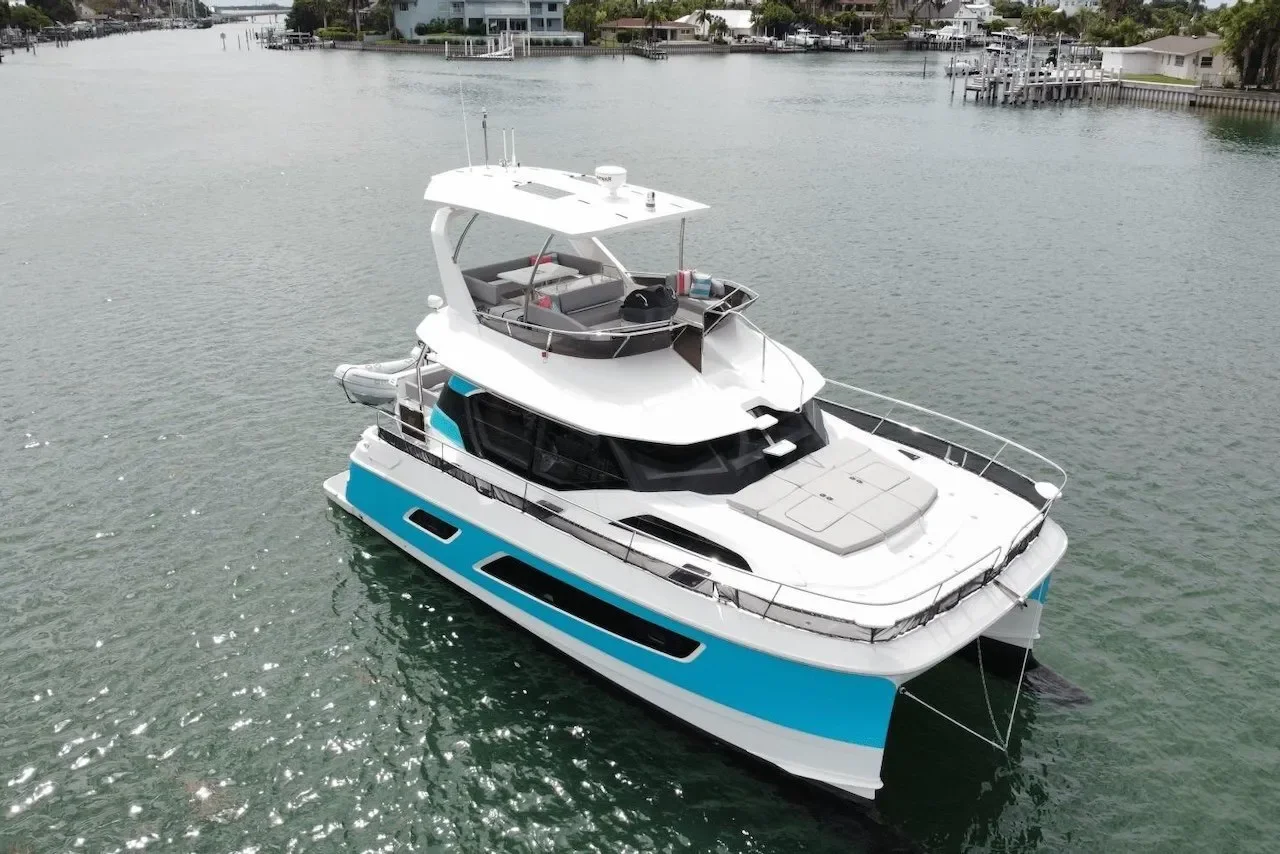 A large white and blue luxury motor yacht anchored in a calm waterway with houses and docks in the background.