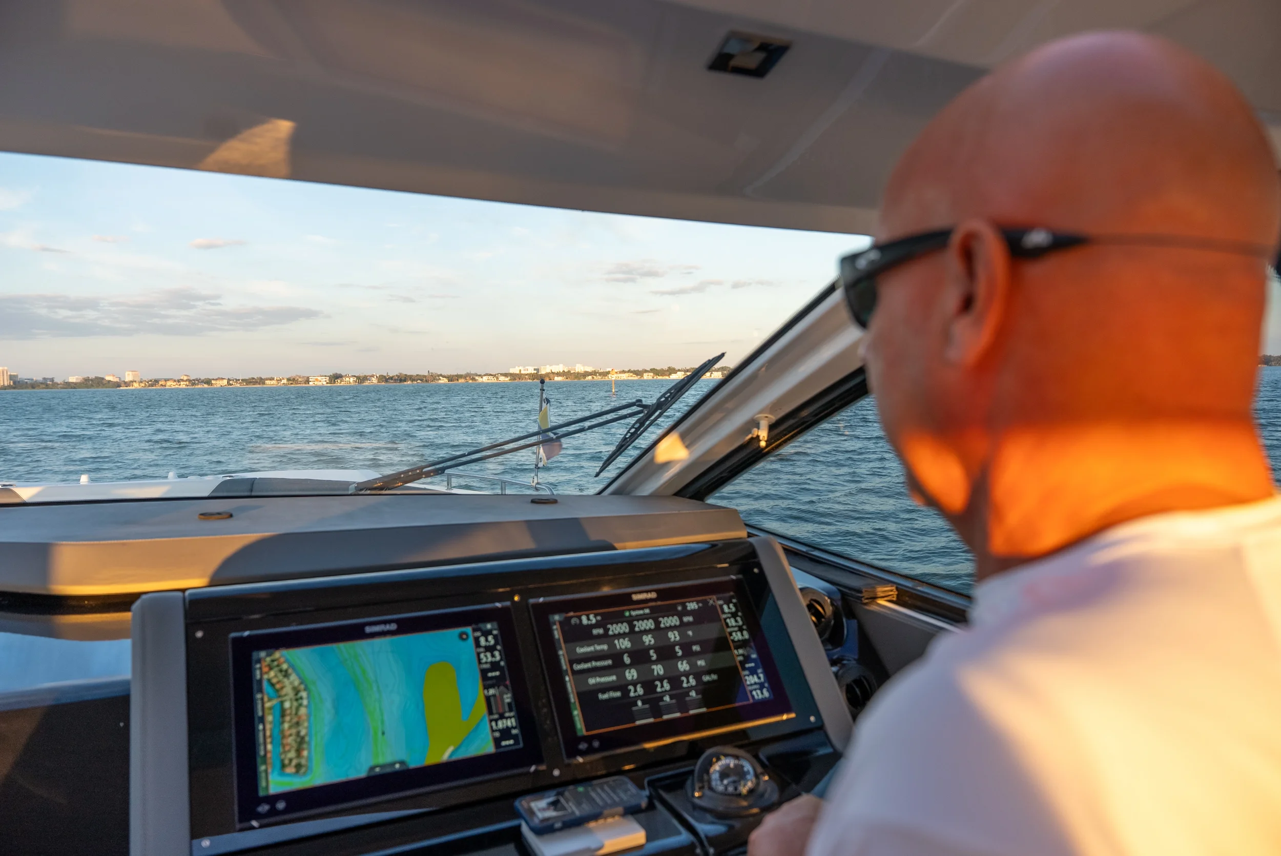 Kokomo charters - St. Pete sunset cruise -  A man steering a boat with a view of water and distant shoreline, using digital navigation screens, in the late afternoon sunlight.