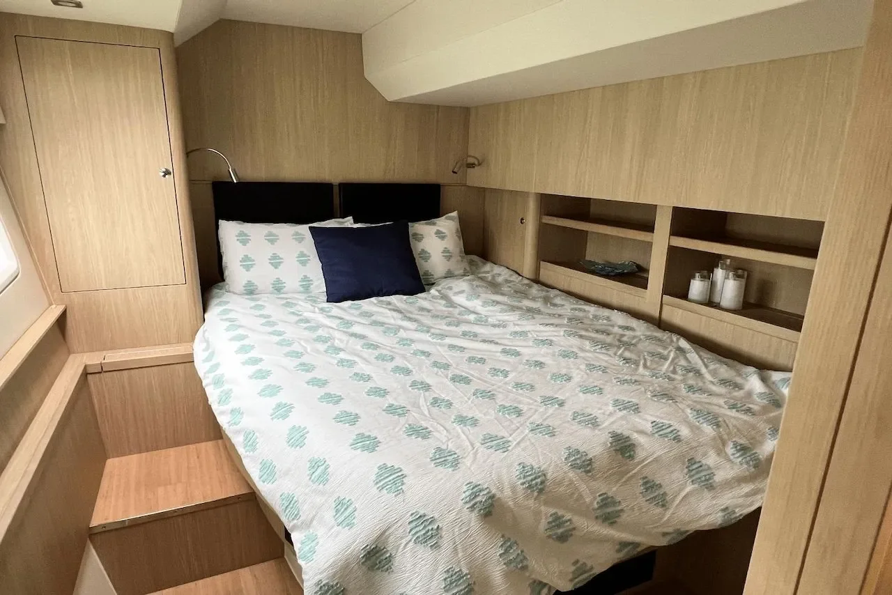 A cozy bedroom with a bed, navy and patterned pillows, built-in wooden shelves, and a wood-paneled wall.