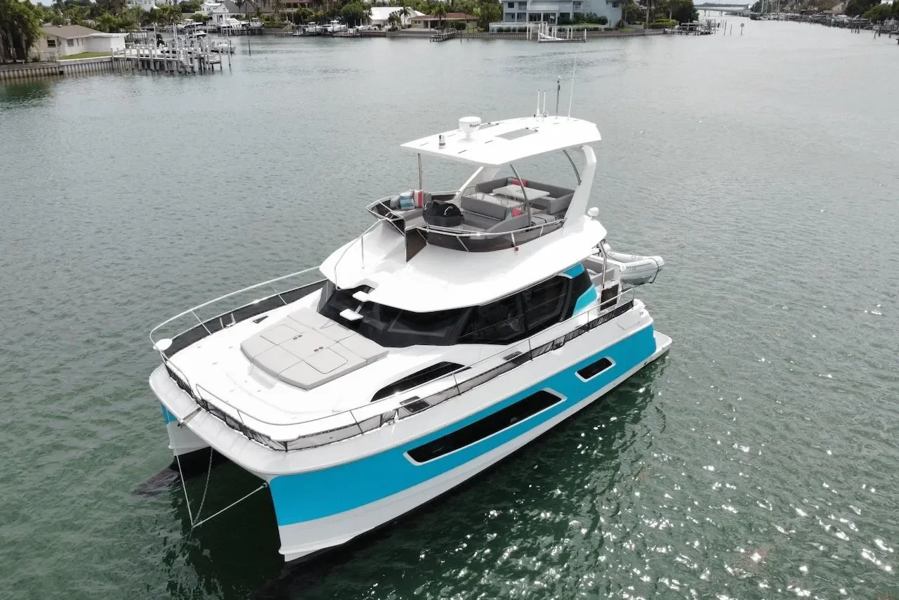 A large white and blue luxury yacht docked in a calm waterway with houses and docks in the background.