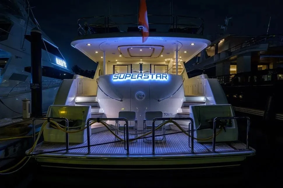 Kokomo charters - Sarasota sunset cruise - A yacht docked at a marina illuminated by blue and white lights, with a neon sign that reads 'SUPERSTAR' on the stern.