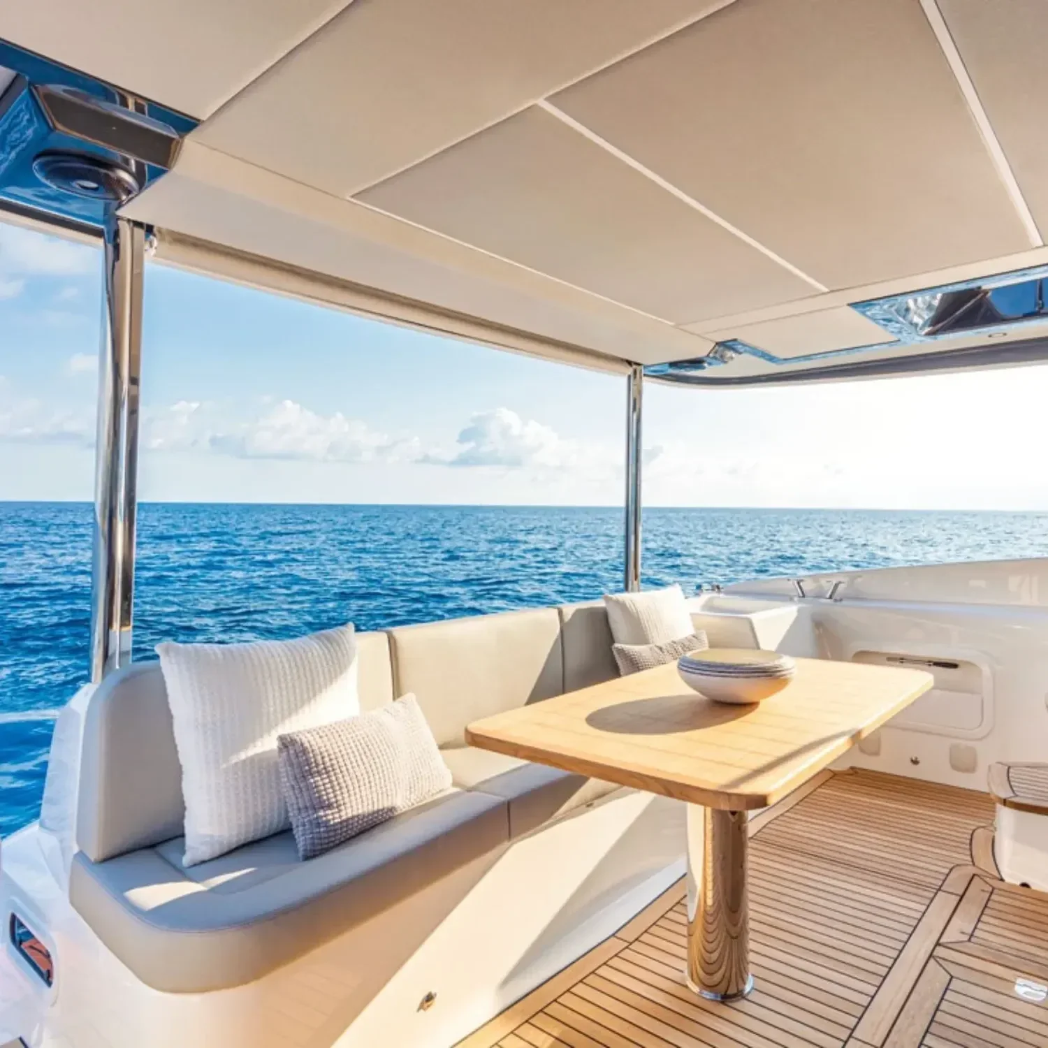 kokomo charters - 52' Rally Point - Luxury yacht with cream-colored cushioned seating, throw pillows, wooden table with bowl, ocean view, blue sky, partially covered deck area