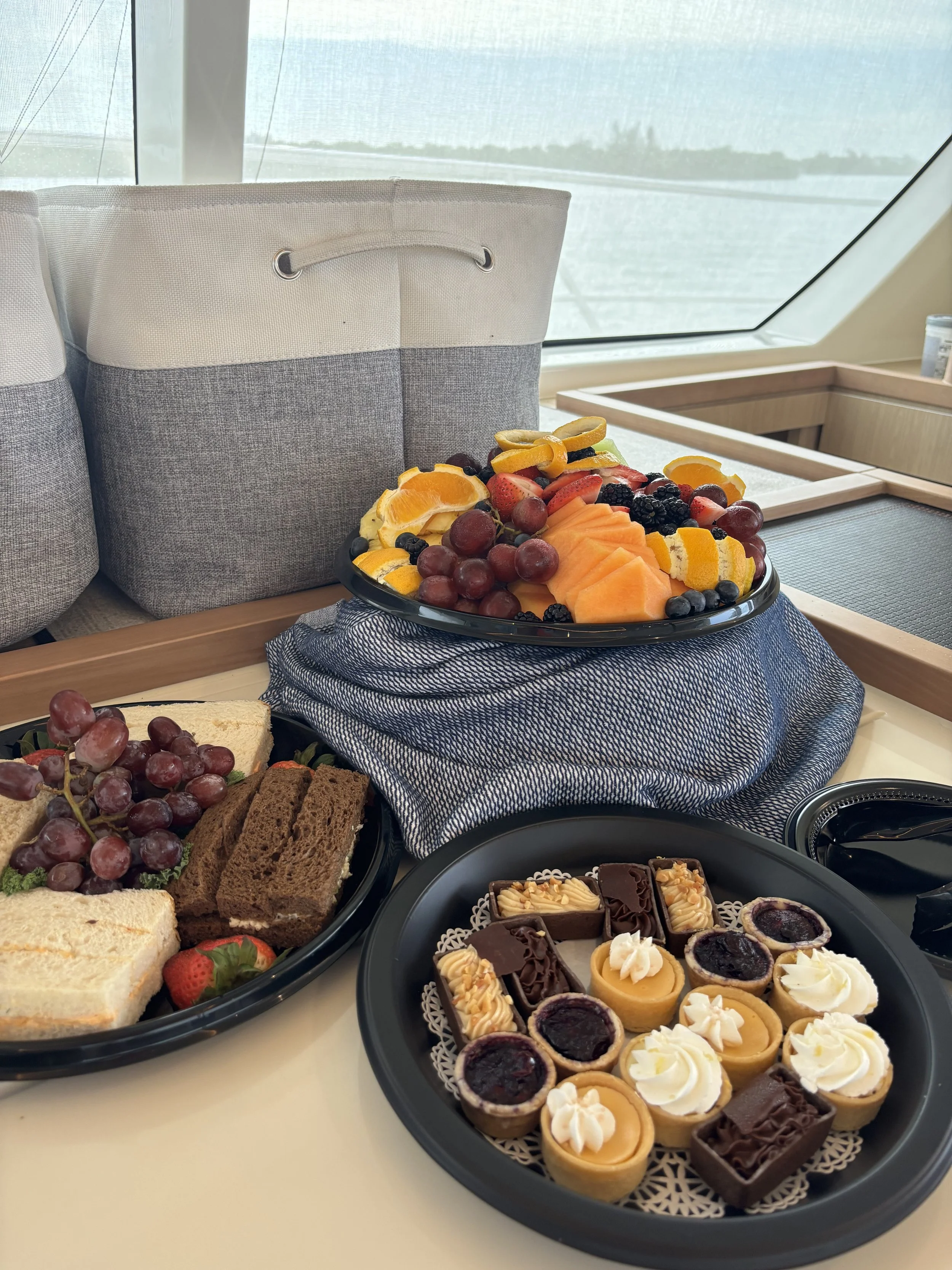 Assorted fruit, sandwiches, and desserts on a boat table.
