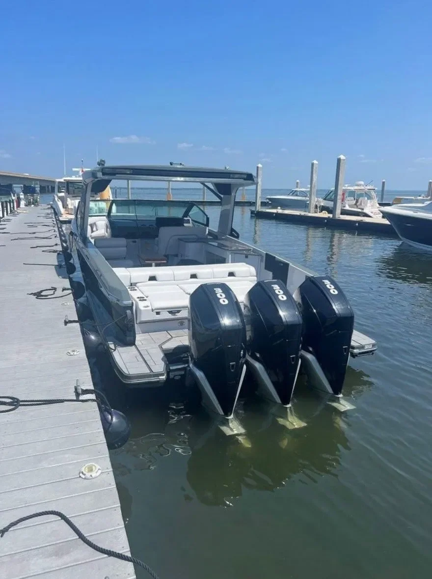 A large motorboat with three Yamaha outboard engines docked at a marina with other boats and a clear blue sky in the background.
