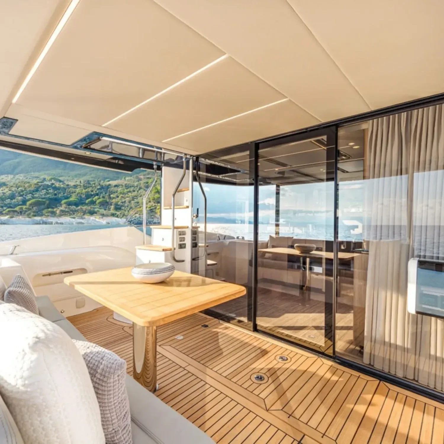 kokomo charters - 52' Rally Point - Luxury yacht's outdoor deck with wooden flooring, a dining table, seating area, and panoramic water and hillside views in the background.