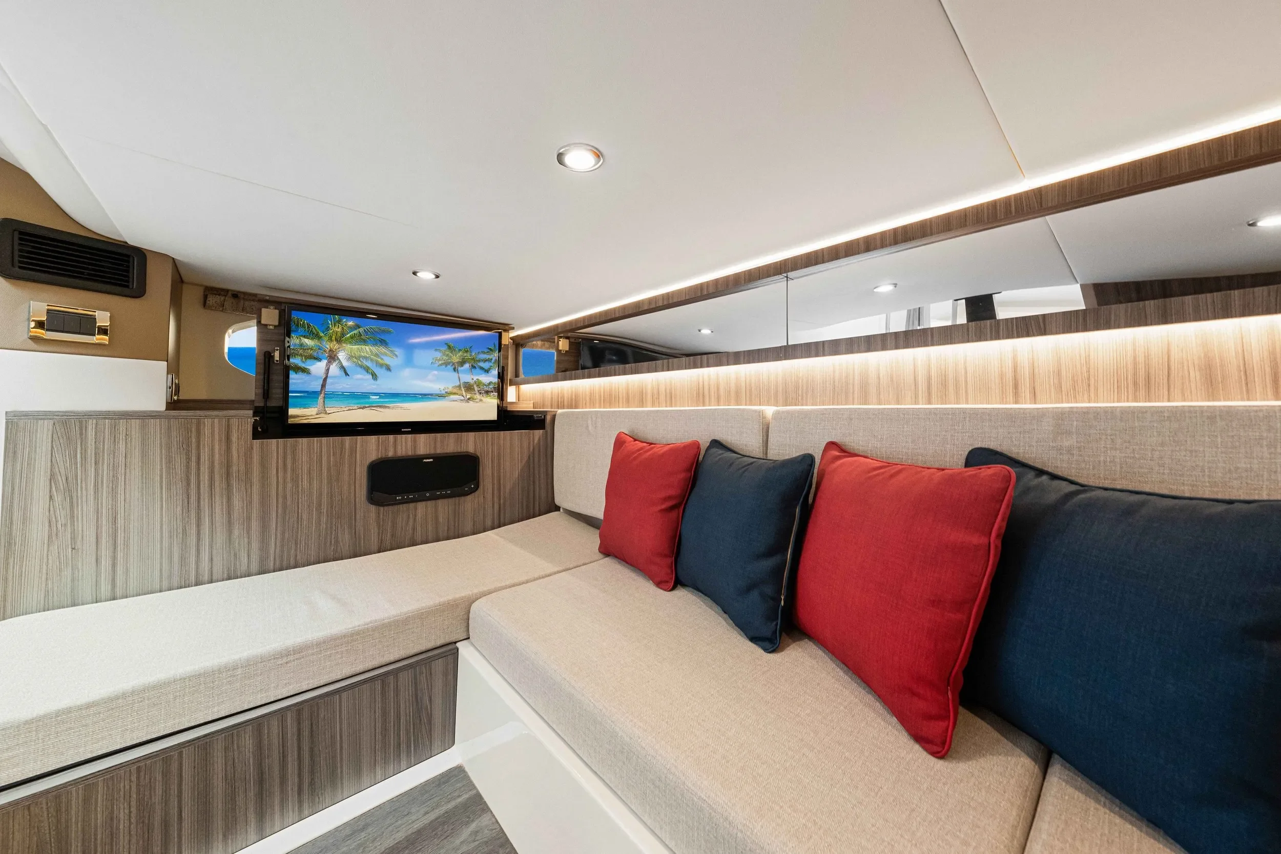 kokomo charters - 40' Golden Ticket - Interior of a yacht or boat with a built-in beige sofa, colorful red and navy pillows, and a flat-screen TV showing a beach scene with palm trees.