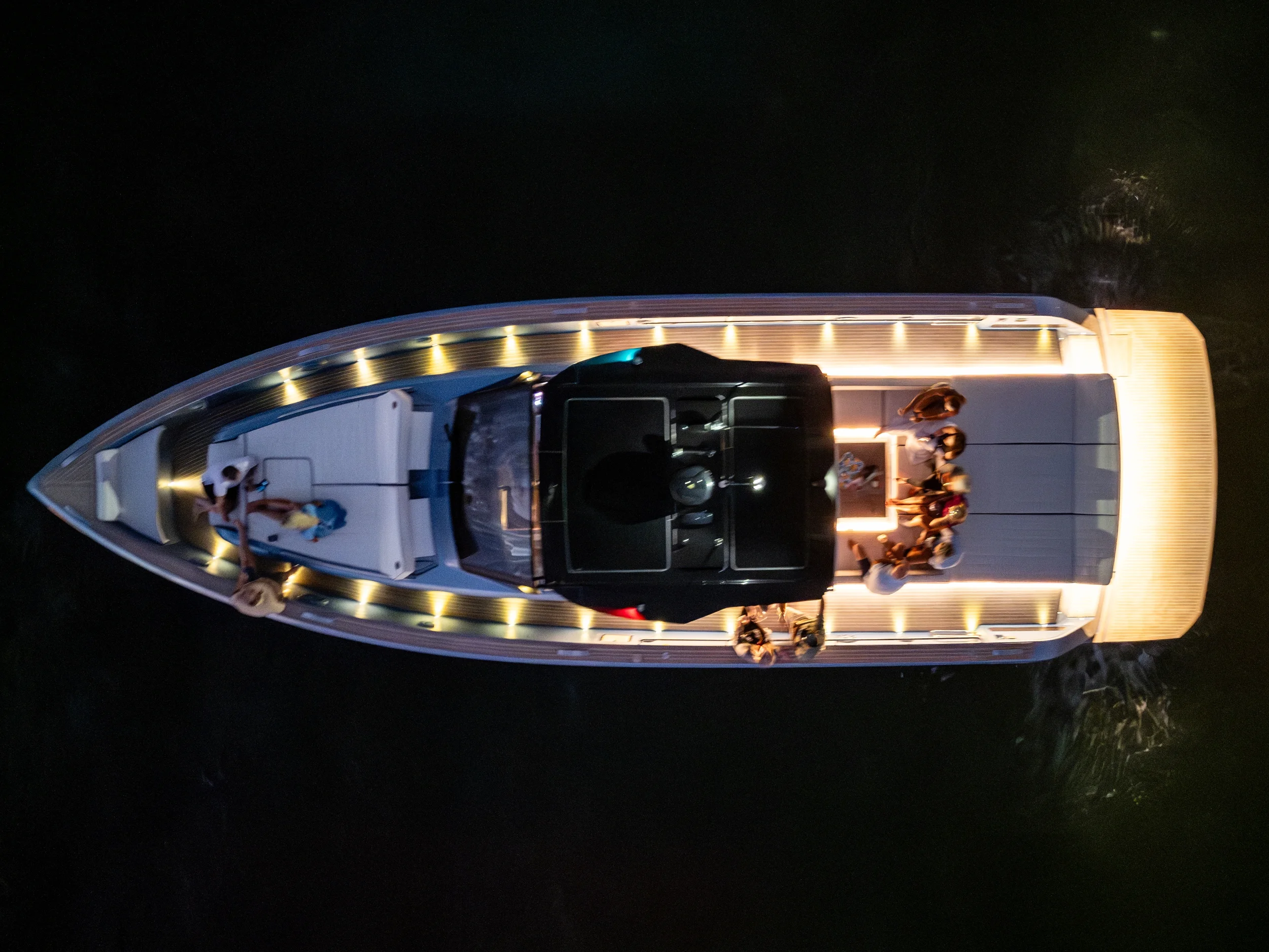 Kokomo charters - yacht float plan Sarasota -Top-down view of a yacht on water at night with people on the deck, illuminated by lights.