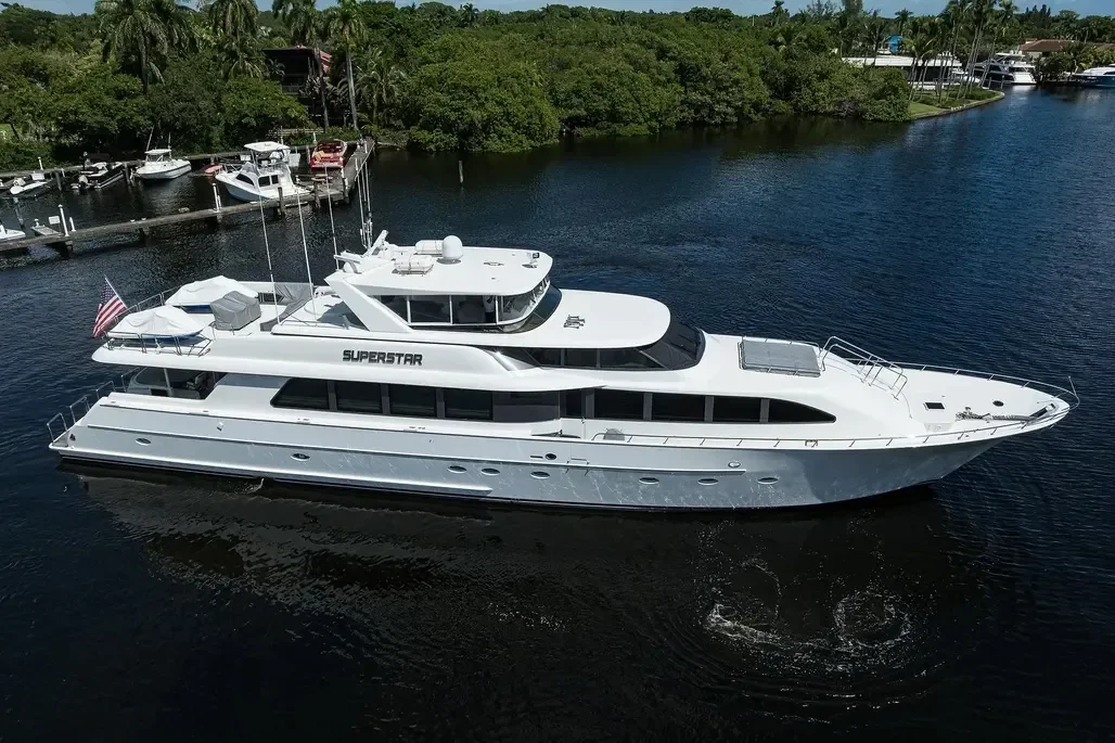 Kokomo Charters - Gulf Coast luxury yacht charter - A large white yacht named 'SUPERSTAR' sailing on a calm river, with green trees and a marina with other boats in the background.