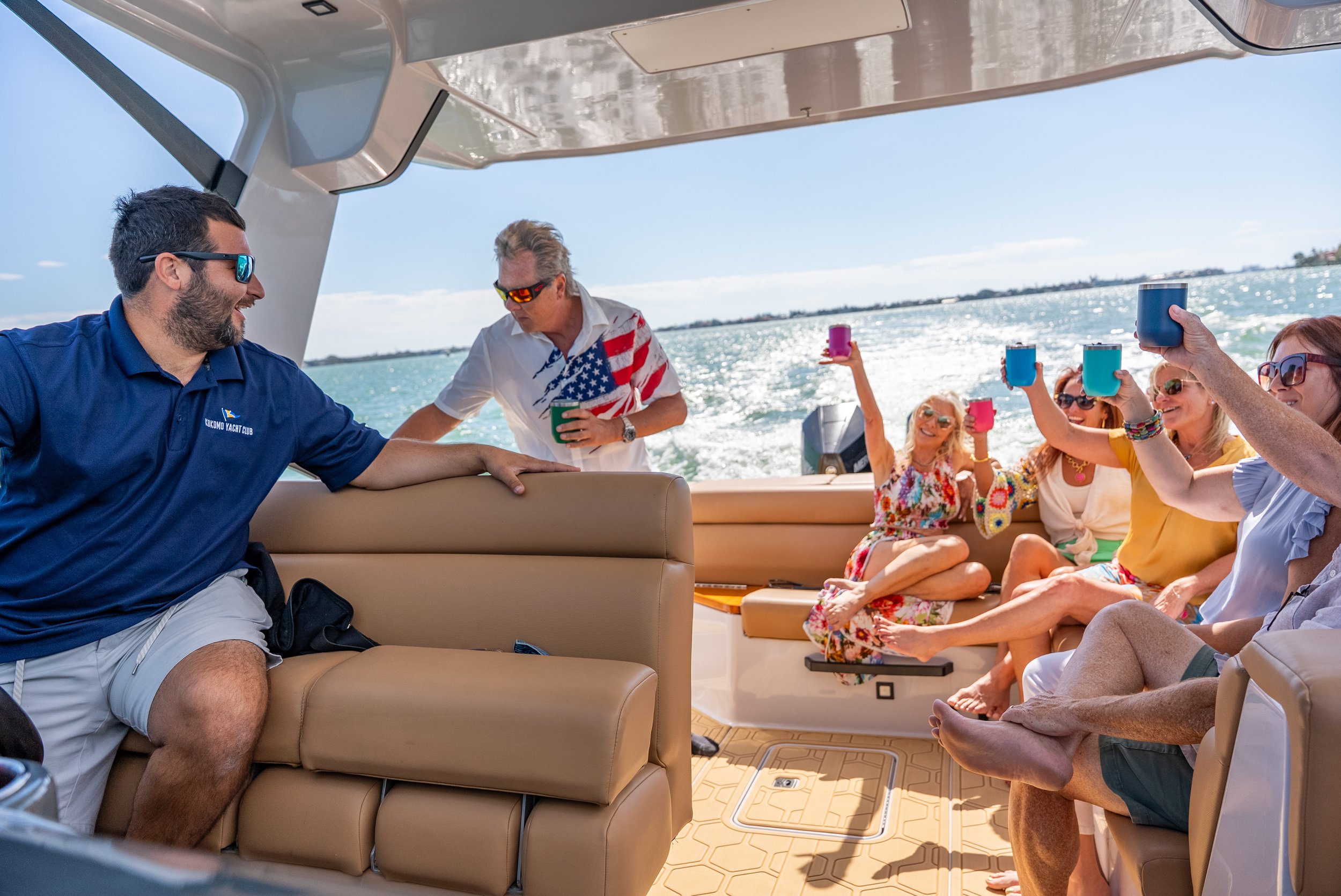 Kokomo charters - yacht float plan Sarasota - A group of people on a boat enjoying sunny weather, holding colorful cups, with water and a clear sky in the background.