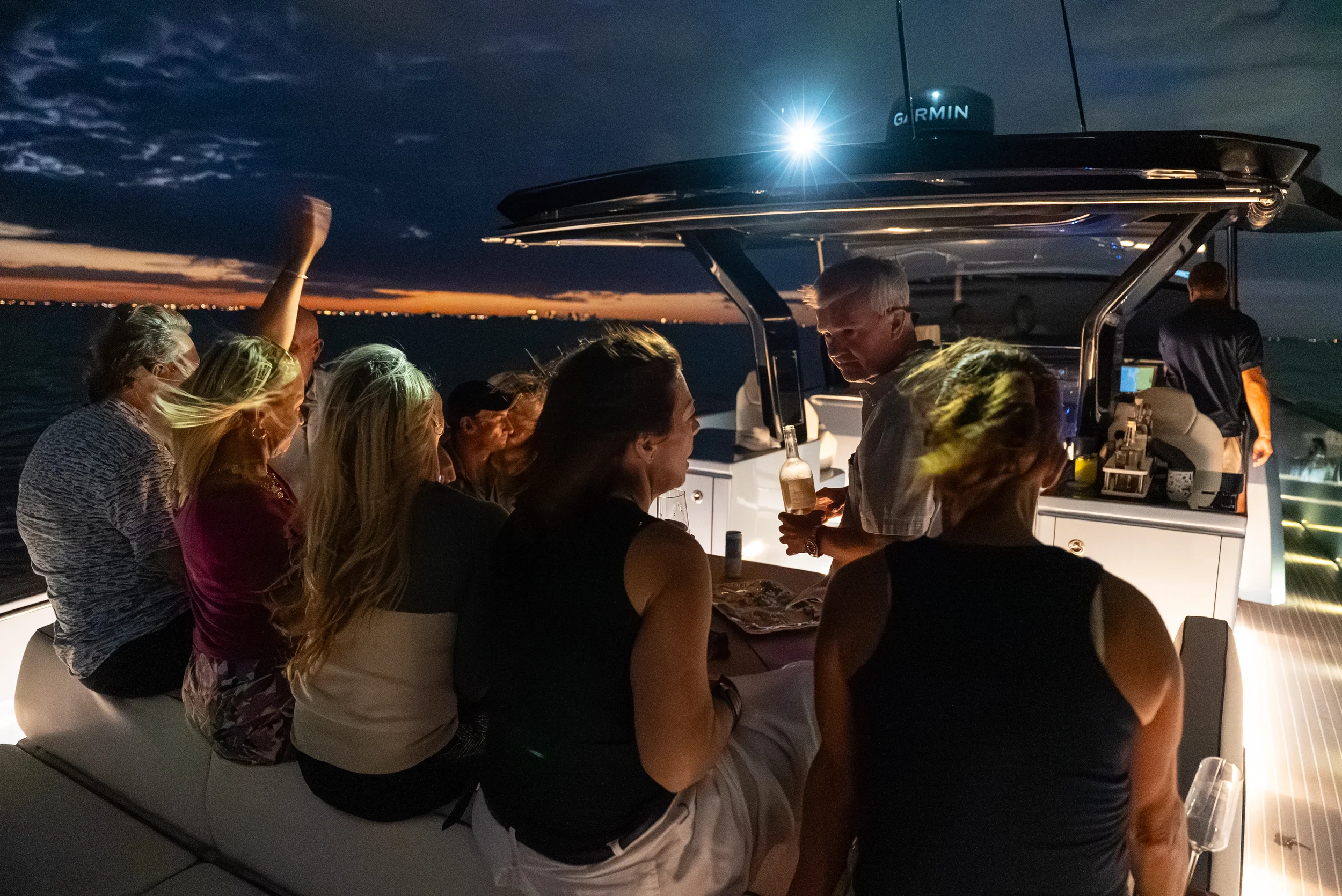 Kokomo charters - yacht float plan Sarasota - People socializing on a boat during sunset, with a bartender serving drinks, and the sky transitioning from sunset to night.