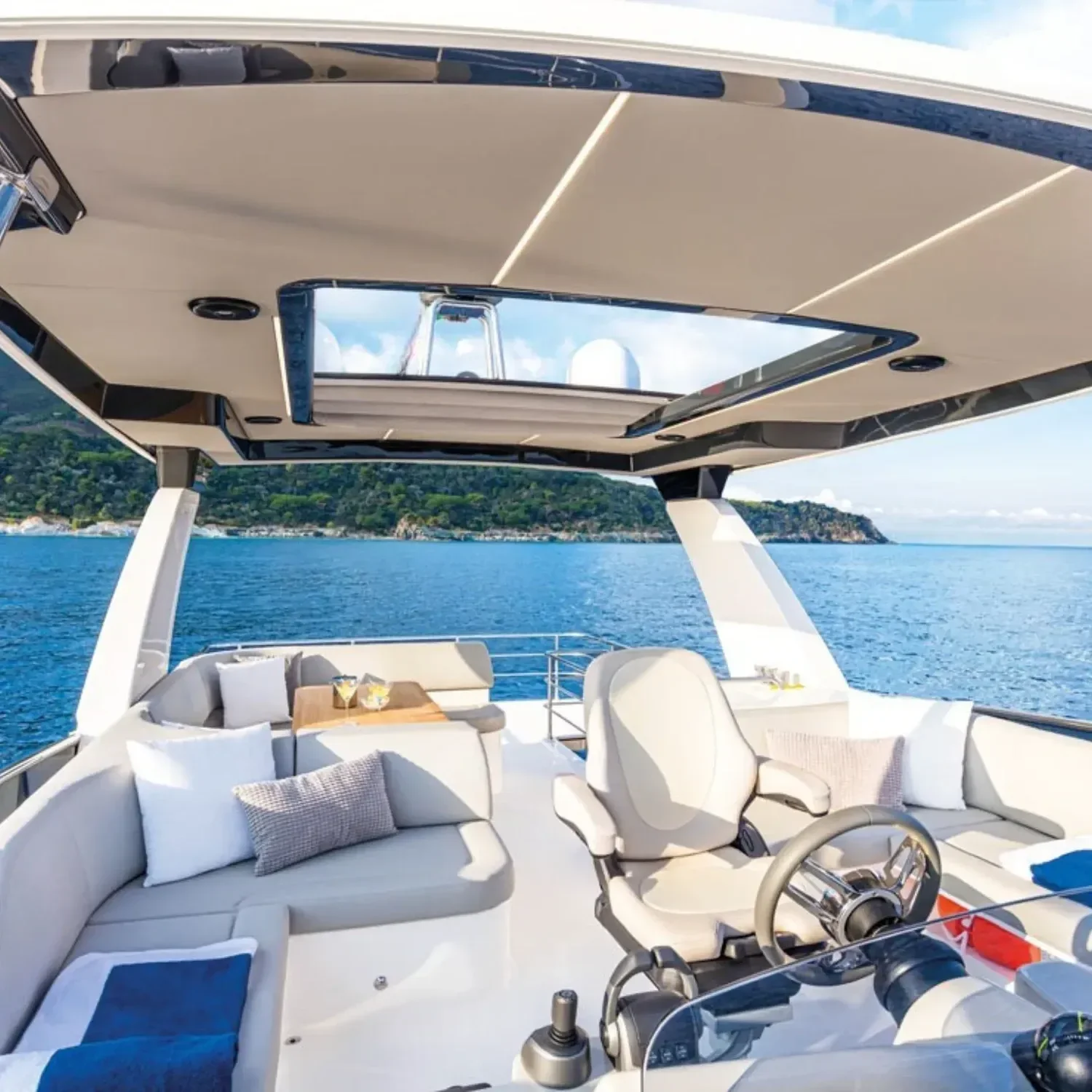 kokomo charters - 52' Rally Point - Deck of a luxury yacht with seating area, pillows, and a captain's chair, overlooking the ocean with a view of green hills and blue sky.