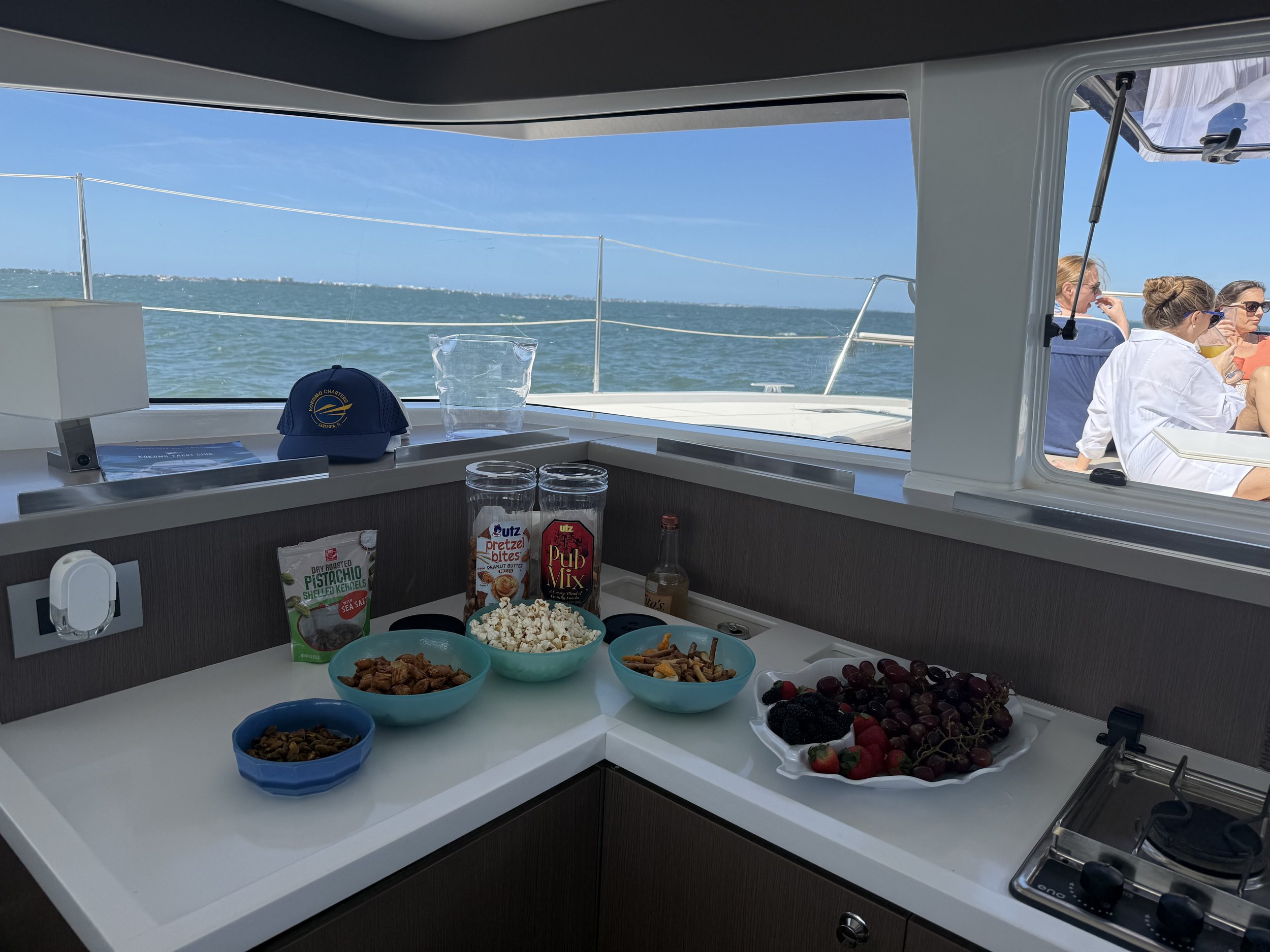 Interior of a boat with snacks and drinks, outdoor view of people relaxing.