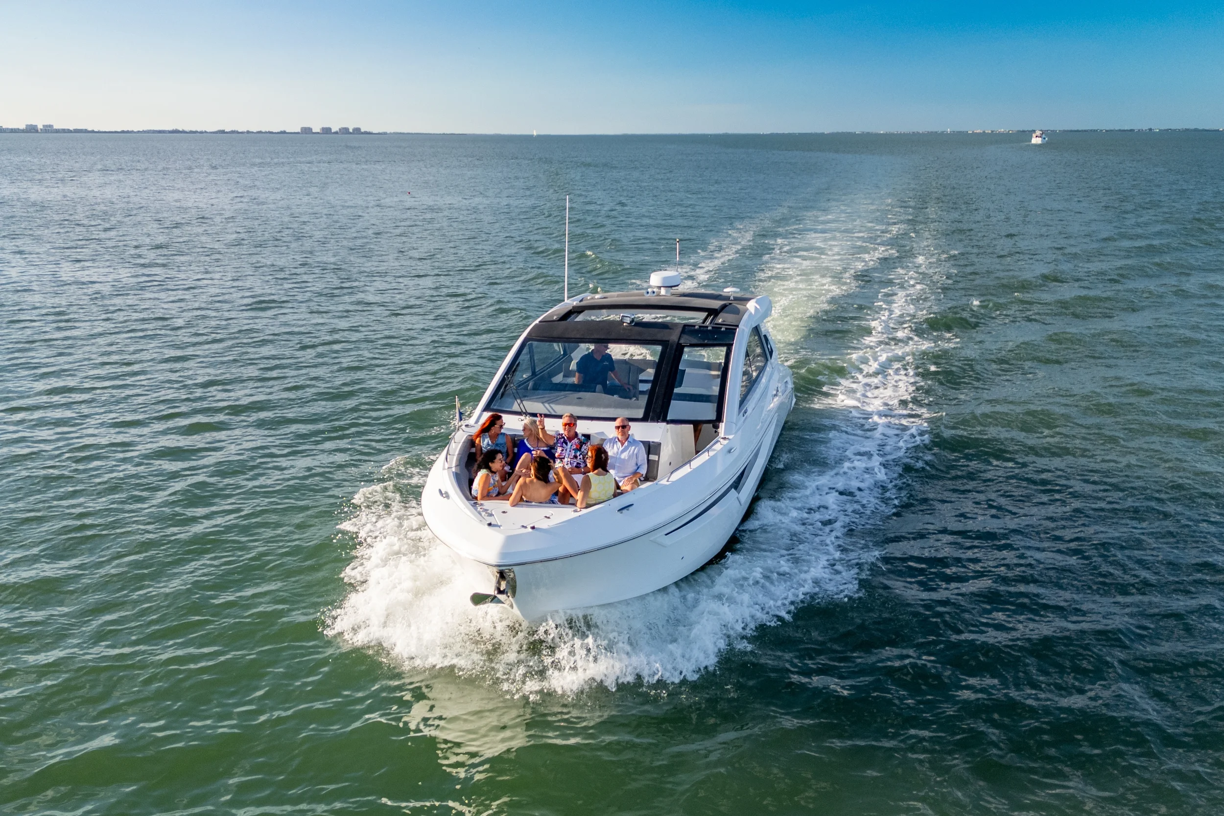 Kokomo charters - luxury yacht charter - A white motorboat with several people on board cruising on a body of water with a city skyline in the background.