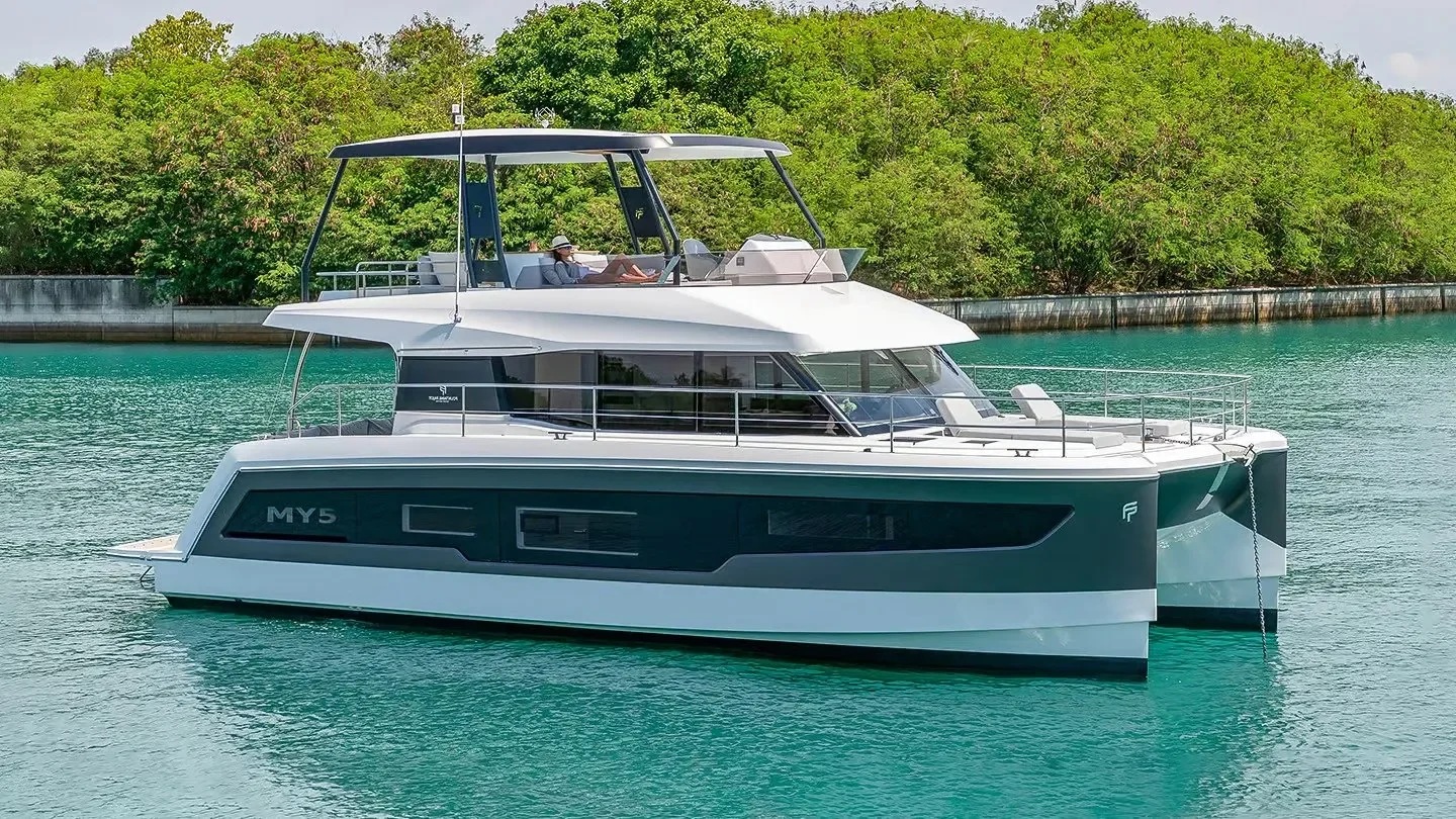 A modern luxury yacht with black and white exterior, docked in turquoise water near a green, wooded shoreline.