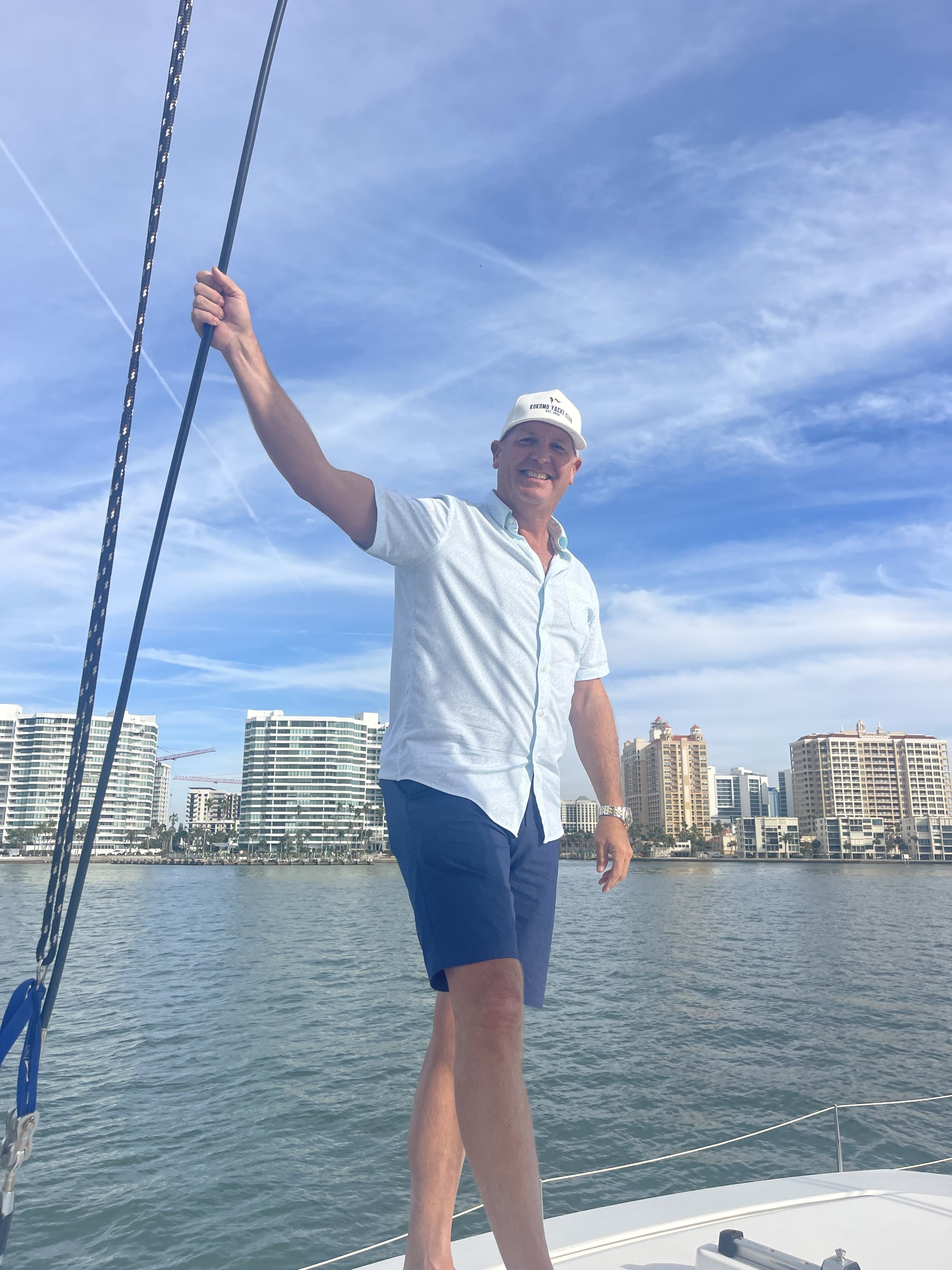 Man on a boat deck holding a rope with cityscape in the background.