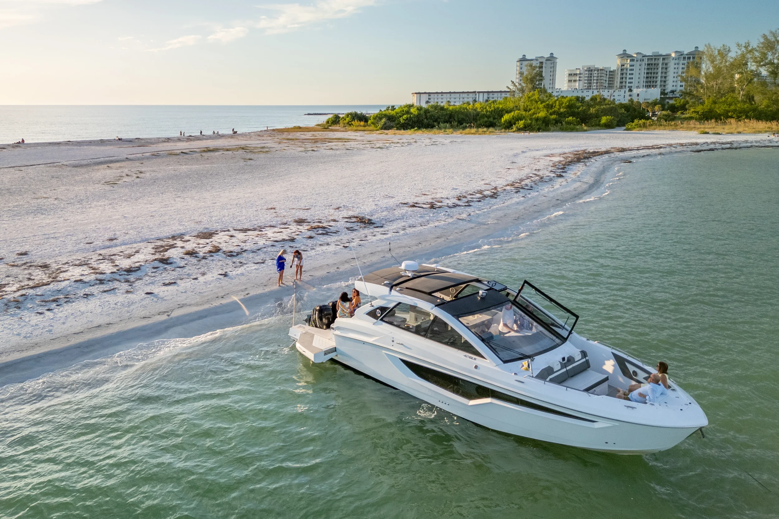 Kokomo charters - Sarasota private yacht charter - A white yacht near a sandy beach with a few people on board and on the shore, and high-rise buildings in the background.