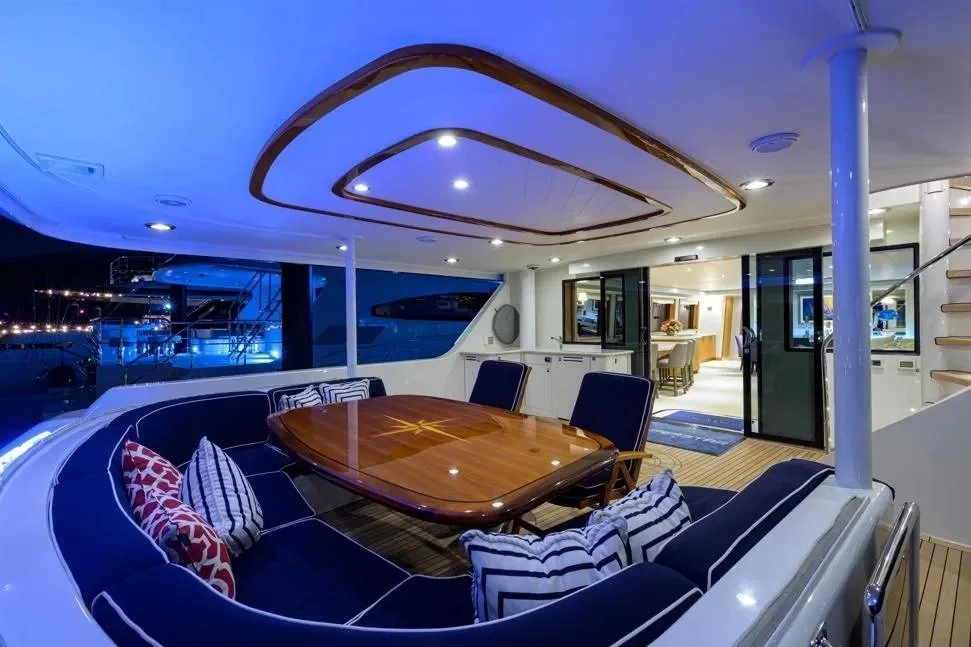 Kokomo charters - Sunset cruises on the Gulf - Outdoor seating area on a yacht with a wooden table, navy blue cushioned seats, patterned pillows, and stairs visible.