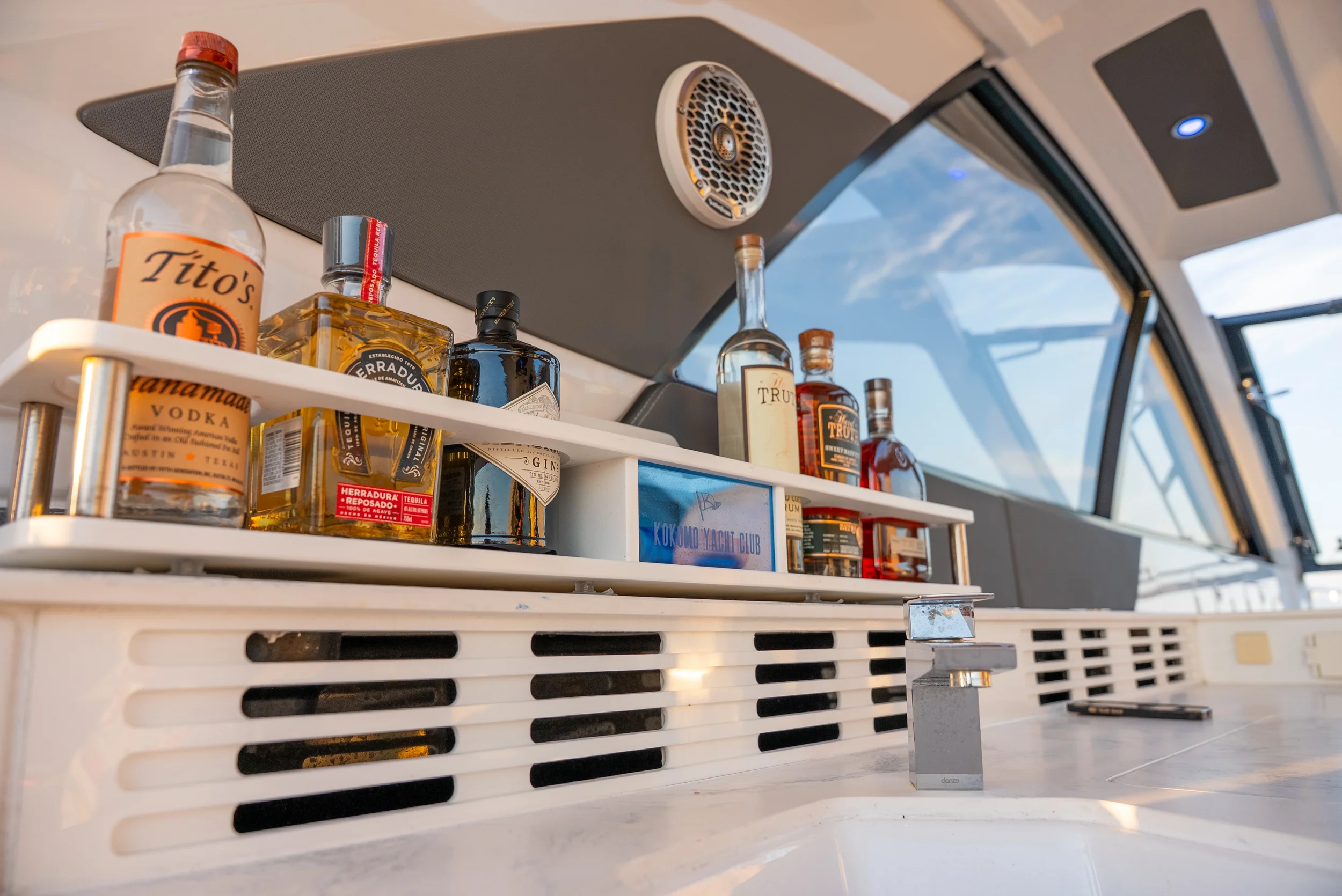 Kokomo charters - St. Pete sunset cruise -  A collection of liquor bottles including Tito's vodka, Herradura Reposado tequila, and other spirits on a white bar counter with a window showing a blue sky with clouds in the background.