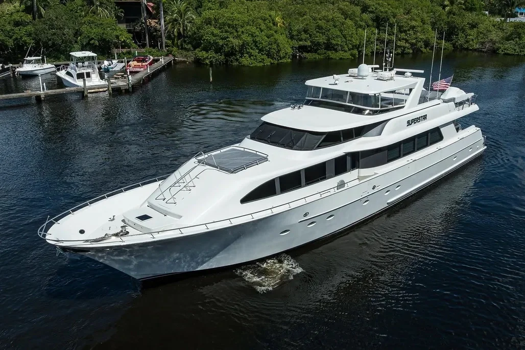 Kokomo charters - Sarasota sunset cruise - Large white yacht named Superstar sailing on calm water near a marina with smaller boats and green trees in the background.