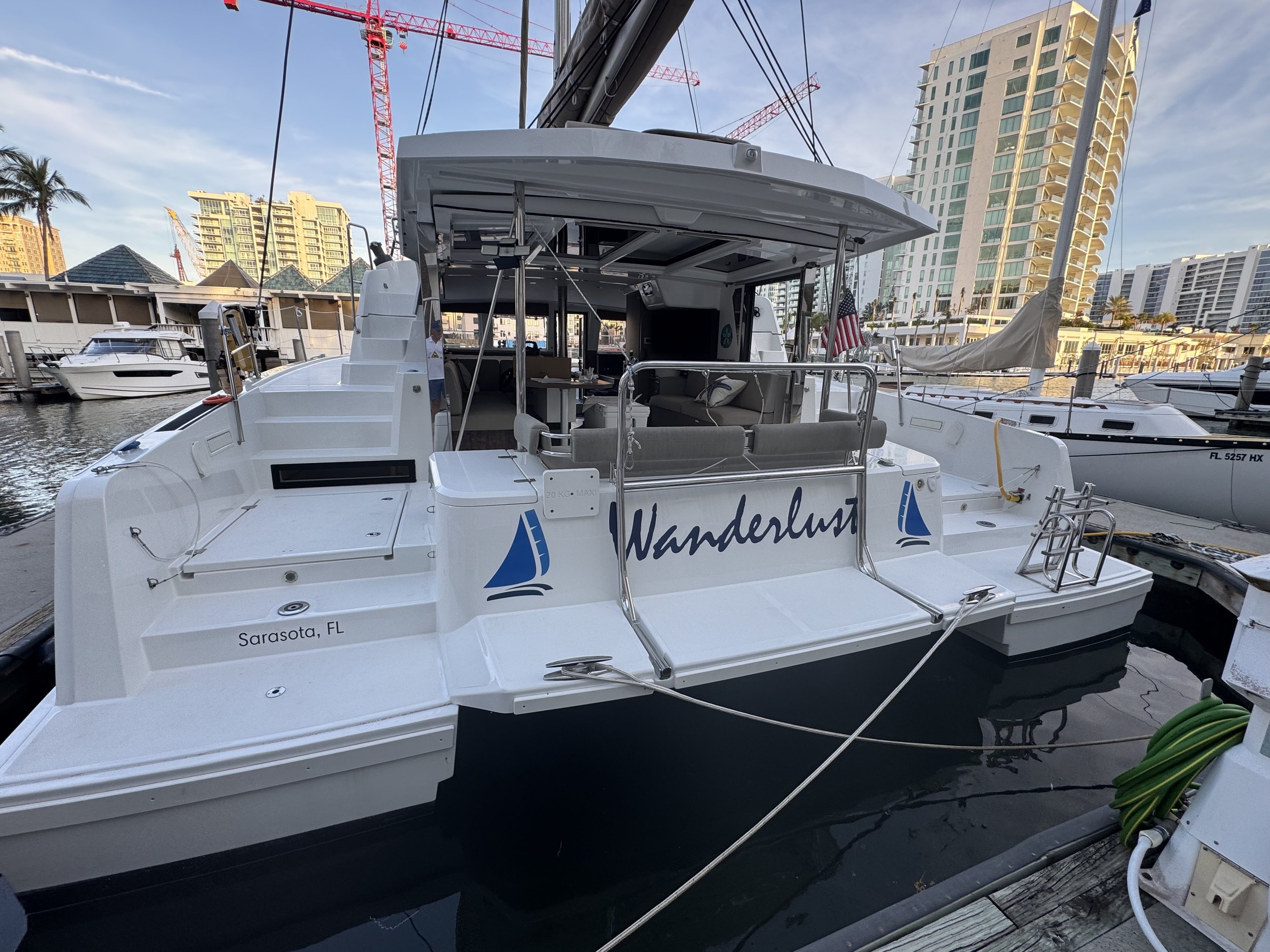 Catamaran named Wanderlust docked at marina in Sarasota, FL with nearby buildings and cranes.