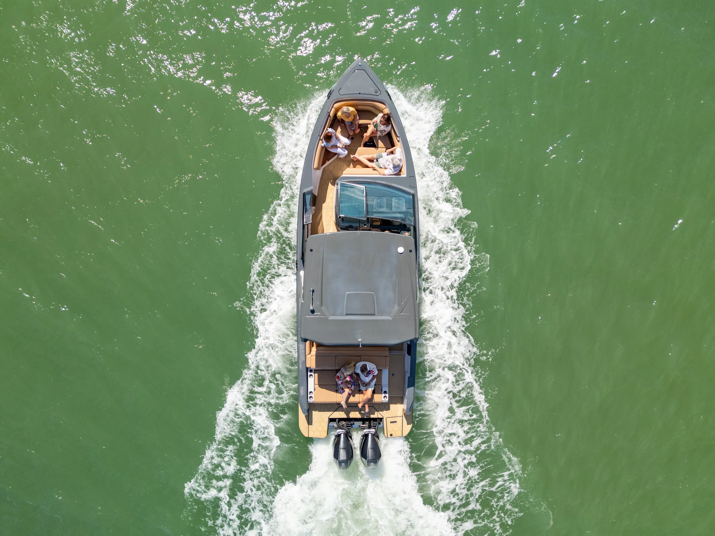 Kokomo charters - yacht float plan Sarasota - Aerial view of a motorboat with people onboard, moving through green water, creating a wake behind it.
