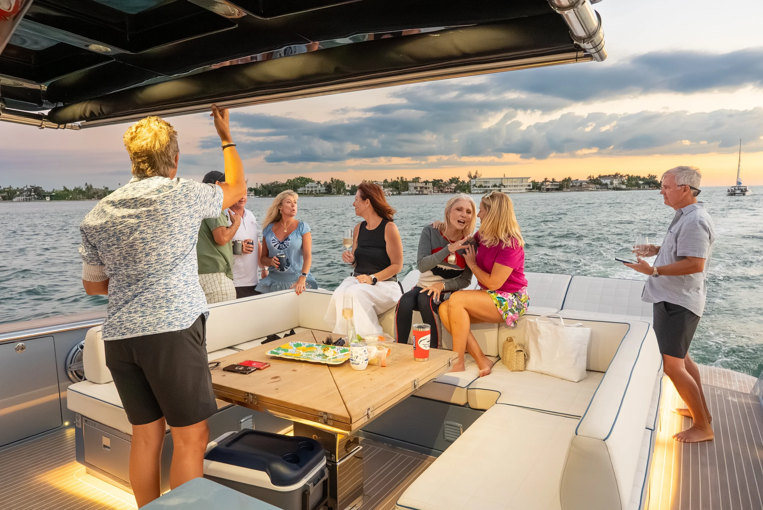Kokomo charters - yacht float plan Sarasota - People enjoying a boat party on a yacht during sunset, with some standing and others sitting on outdoor seating, holding drinks, and engaging in conversation.