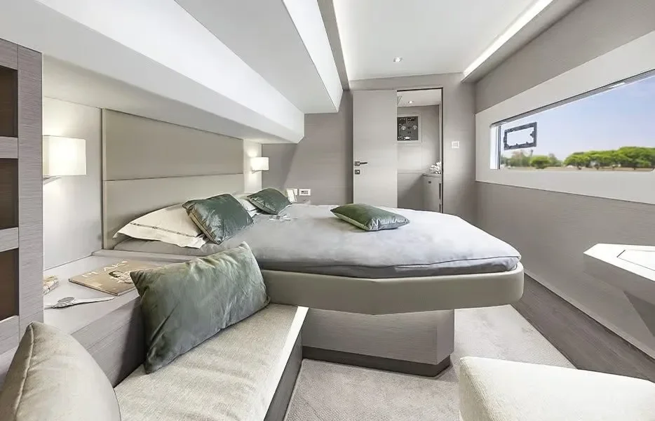 Modern, minimalist hotel room with a large bed, green and white pillows, a window showcasing a blue sky and trees, and a seating area with a bench and pillows.