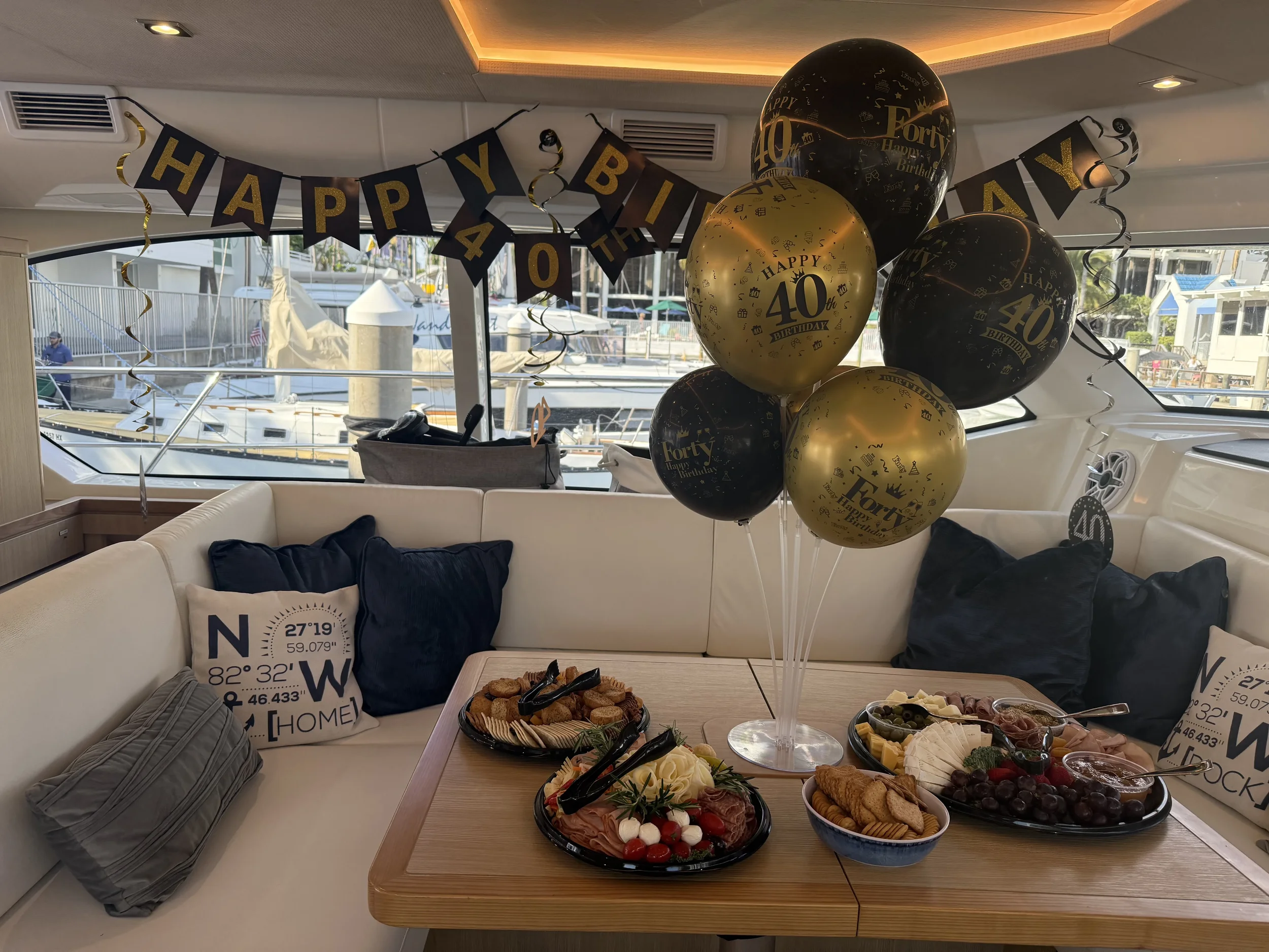 kokomo charters - 50' Memory Maker - View of the back deck of a boat with white cushioned seating, a central table with a yellow flower arrangement, and a scenic water and tree-lined shoreline in the background.