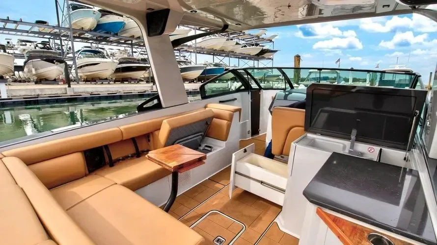 kokomo charters - 35' Ocean Rode - Interior of a boat with tan leather seating, a small wooden table, and a view of a boat marina with multiple boats docked.