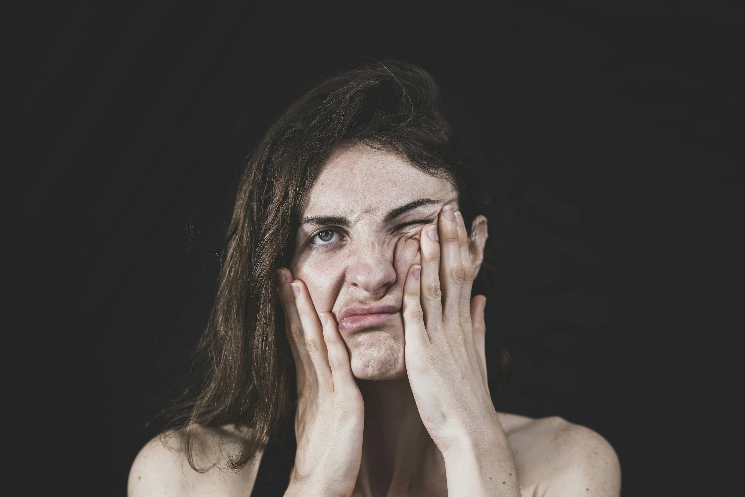 Persona expresando frustración y cansancio, con las manos en el rostro, sobre fondo negro. Simboliza los problemas emocionales.