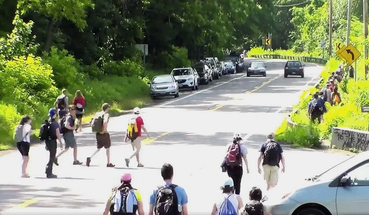Groups of people walking across busy Route 9D toward Breakneck Ridge, with cars parked on the side, and oncoming traffic down the road.