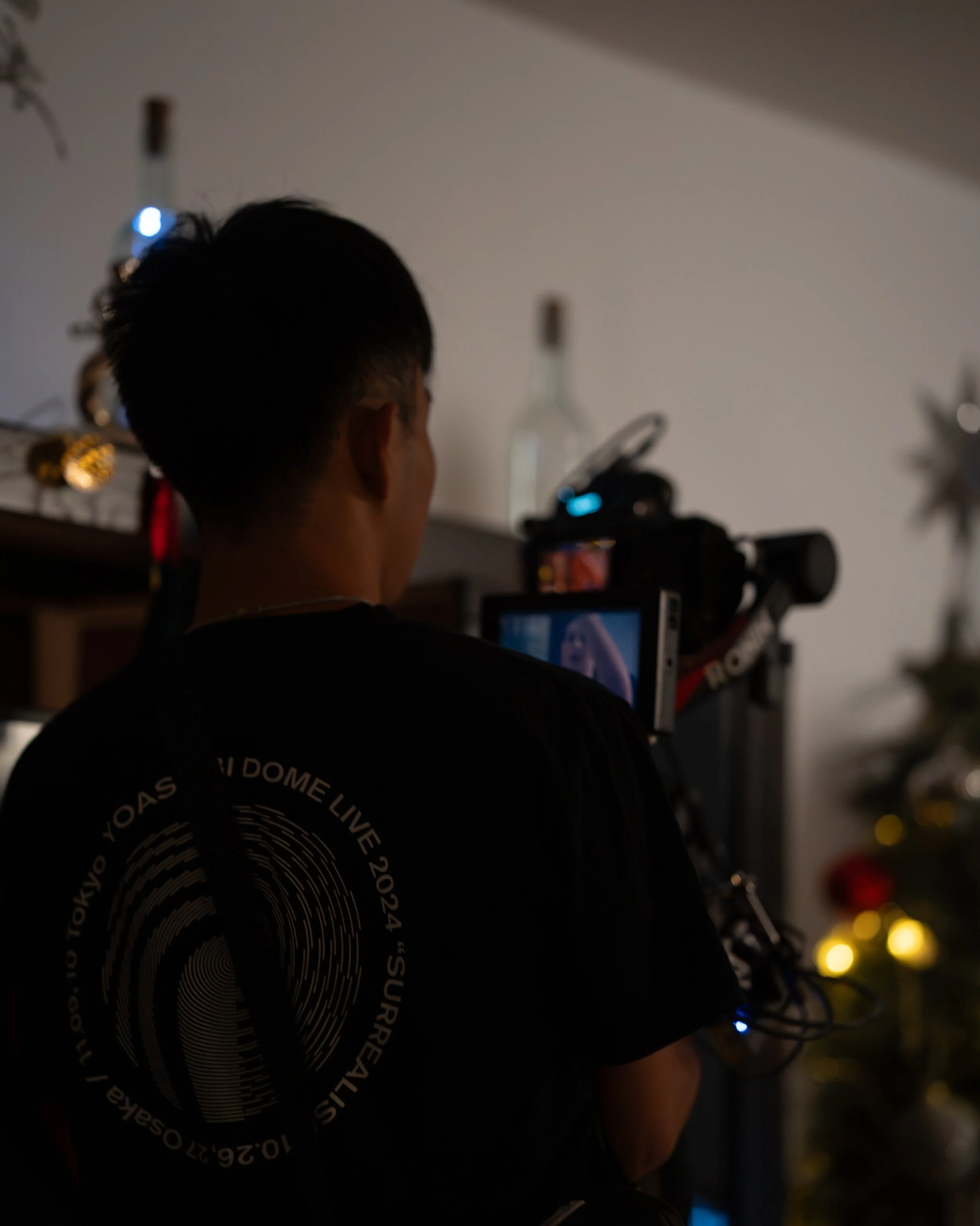 Person standing in front of a camera filming indoors, with a Christmas tree visible in the background.