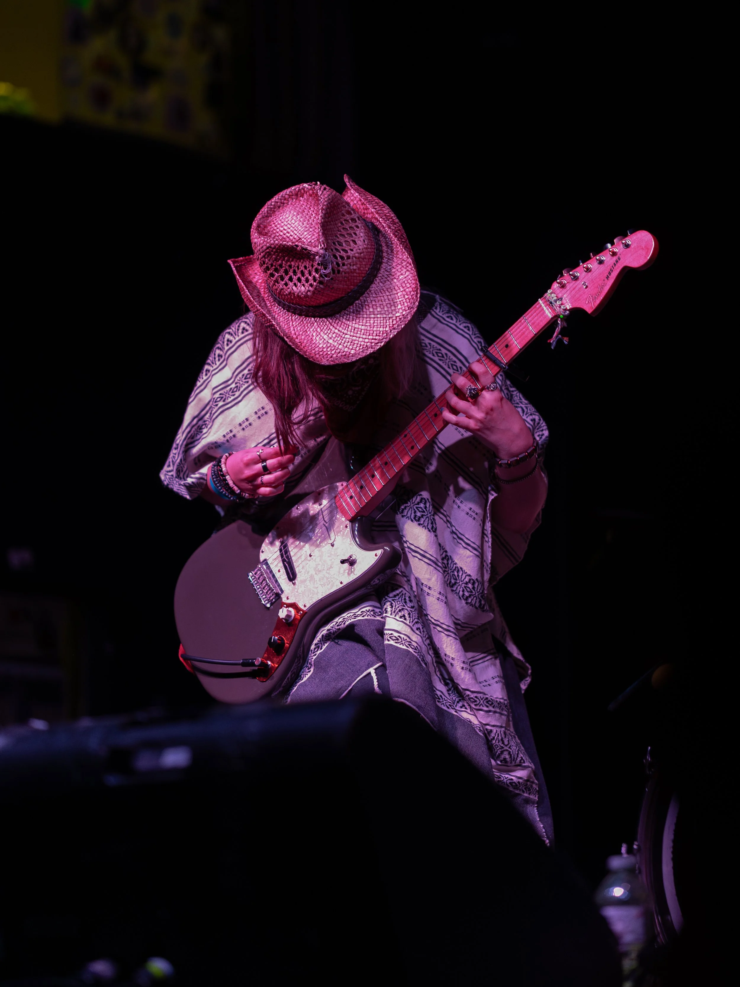 Musician wearing a pink hat playing an electric guitar on stage.