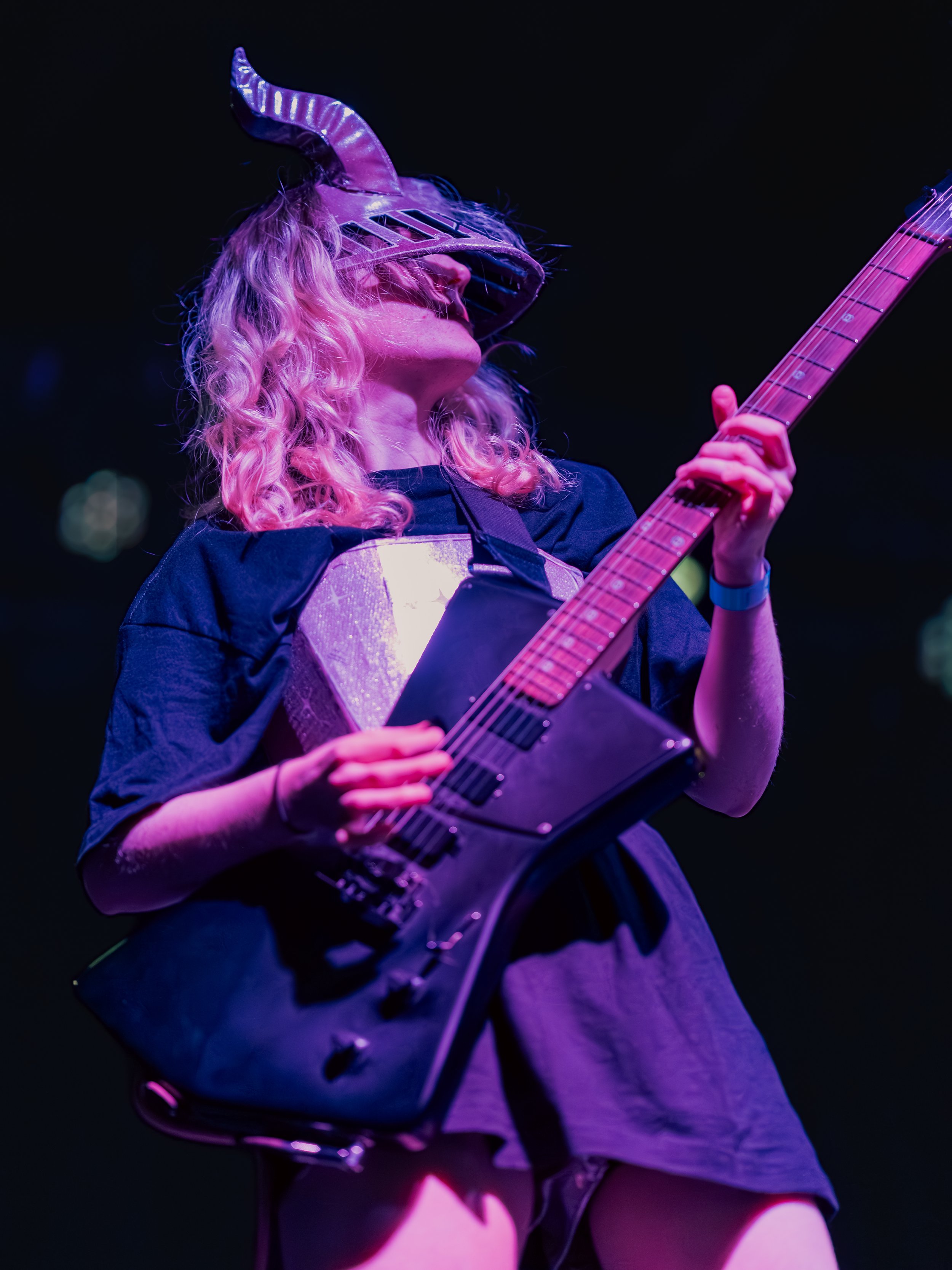 Person wearing a horned mask and playing electric guitar on stage.