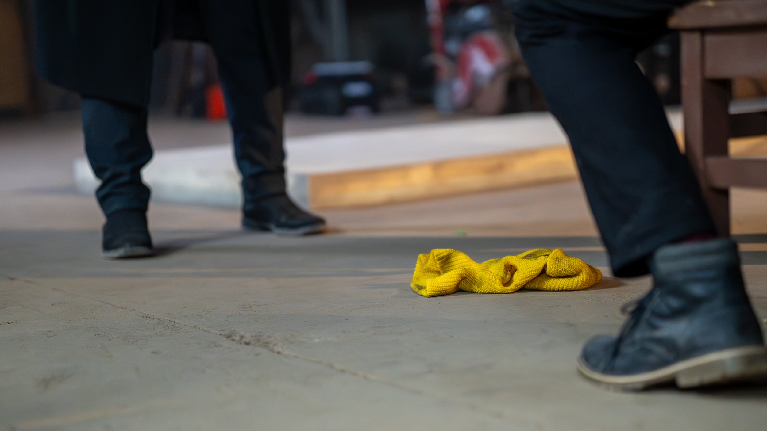 Close-up of a construction site floor with black boots on either side and a yellow cloth on the ground.