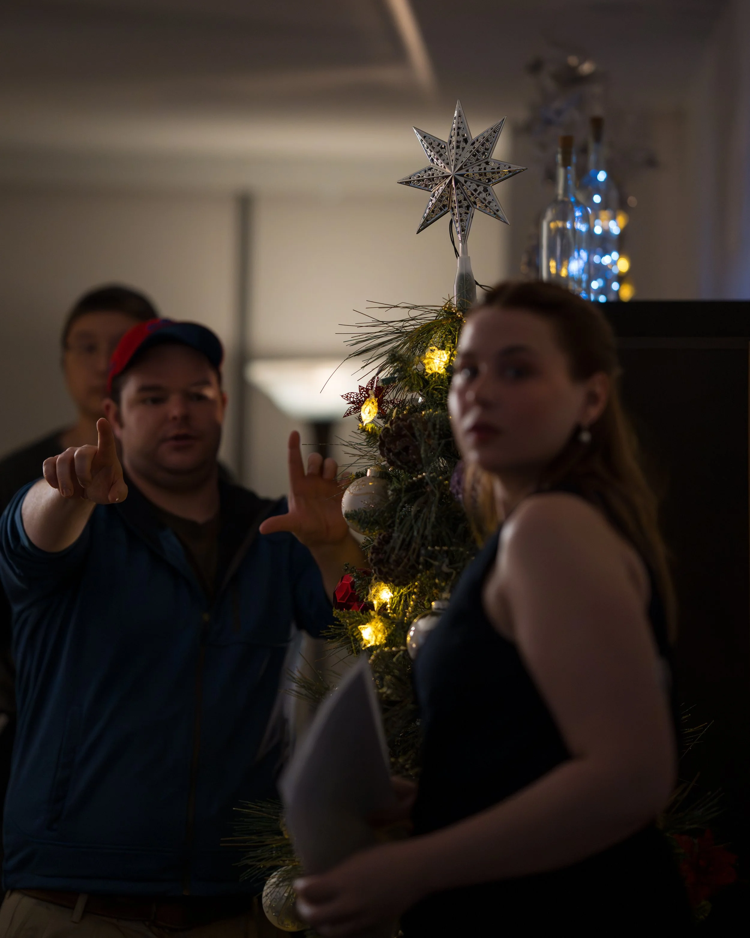 People decorating a Christmas tree with ornaments and lights, with a star topper, in a festive indoor setting.
