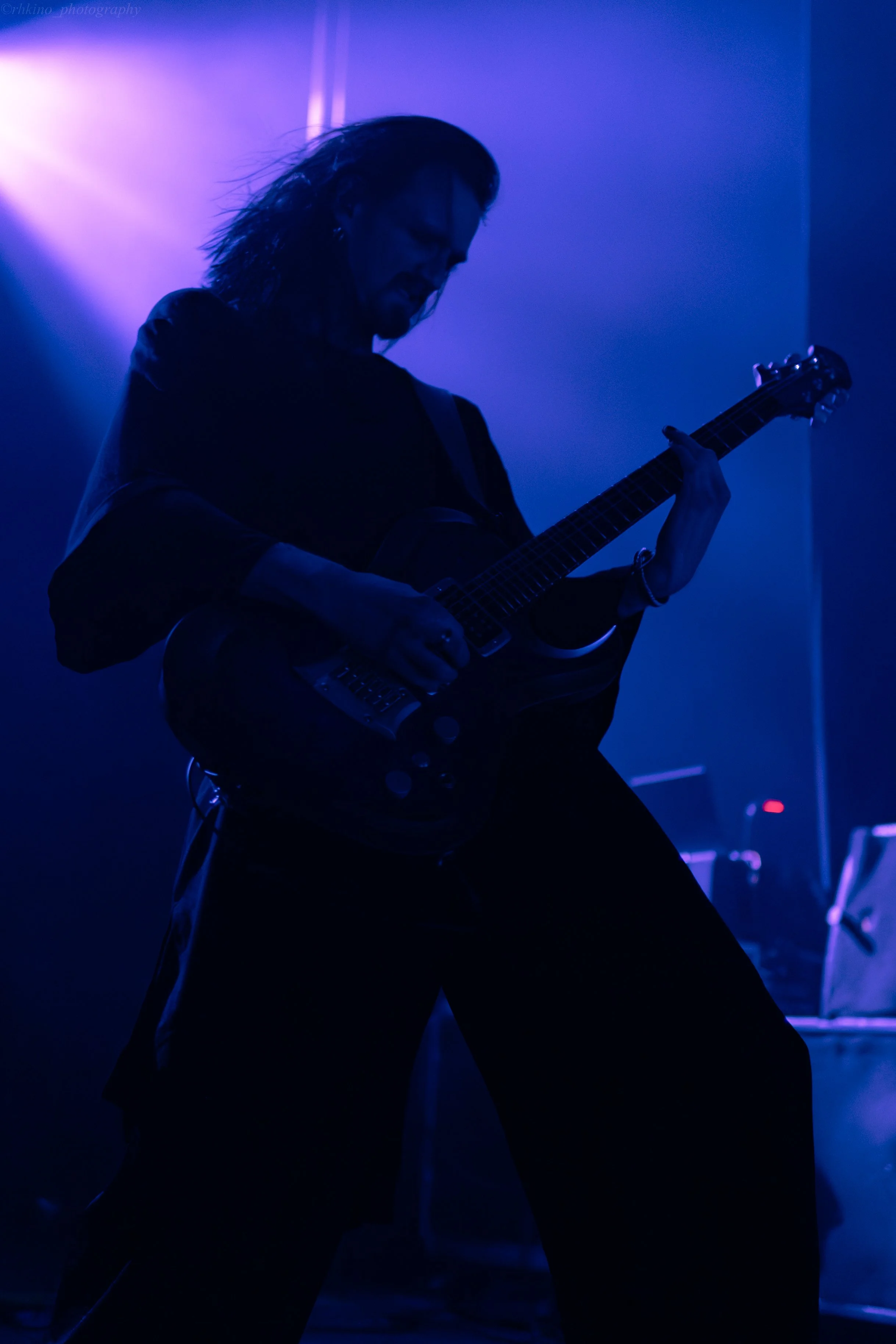 A guitarist playing on stage with blue and purple stage lighting, creating a silhouette effect.
