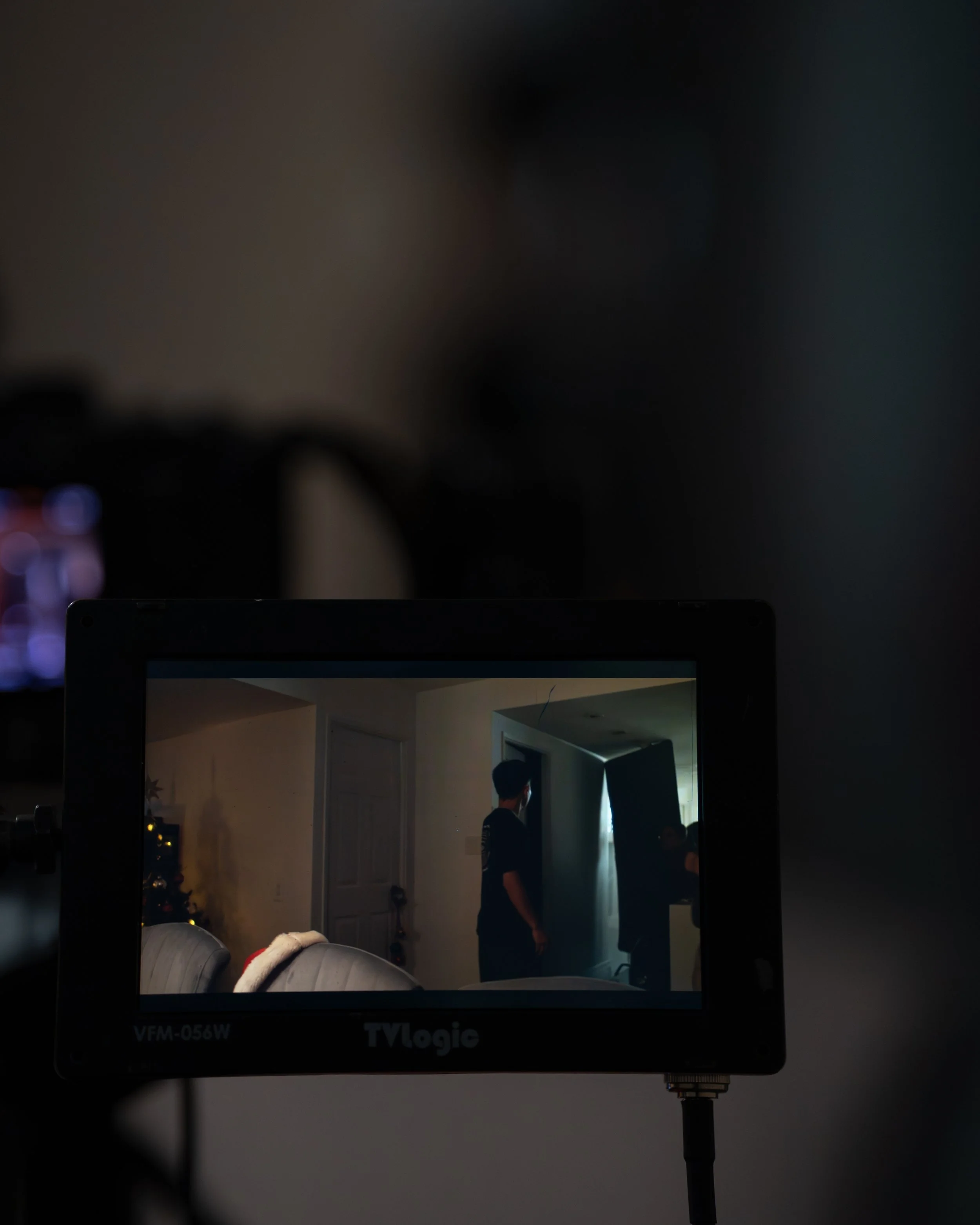 A TV monitor shows a person standing in a living room near a doorway, with a Christmas tree decorated with lights in the background.