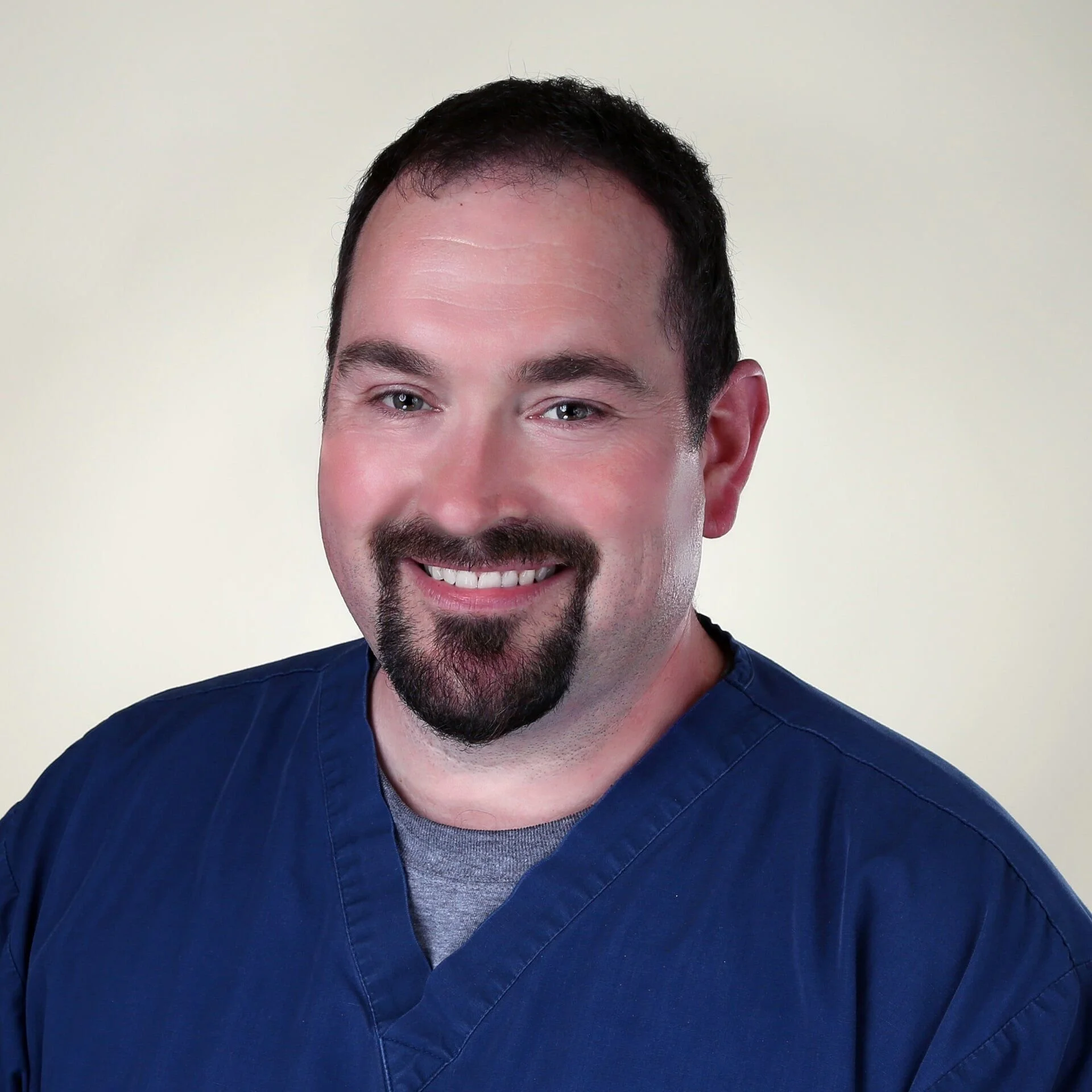 Portrait of a smiling man wearing blue medical scrubs.