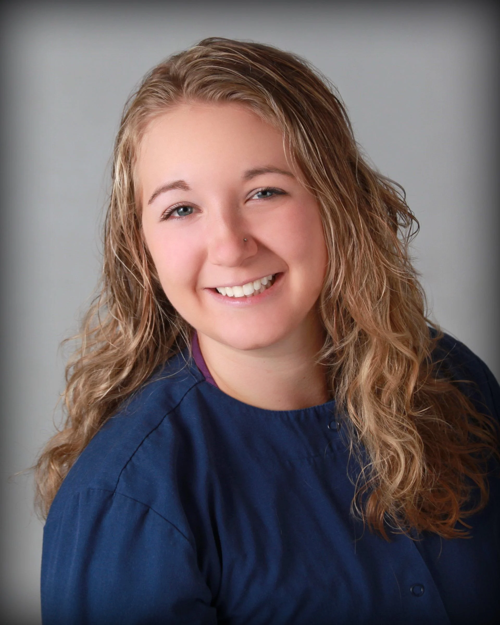 Smiling woman with wavy blonde hair wearing a dark blue top.