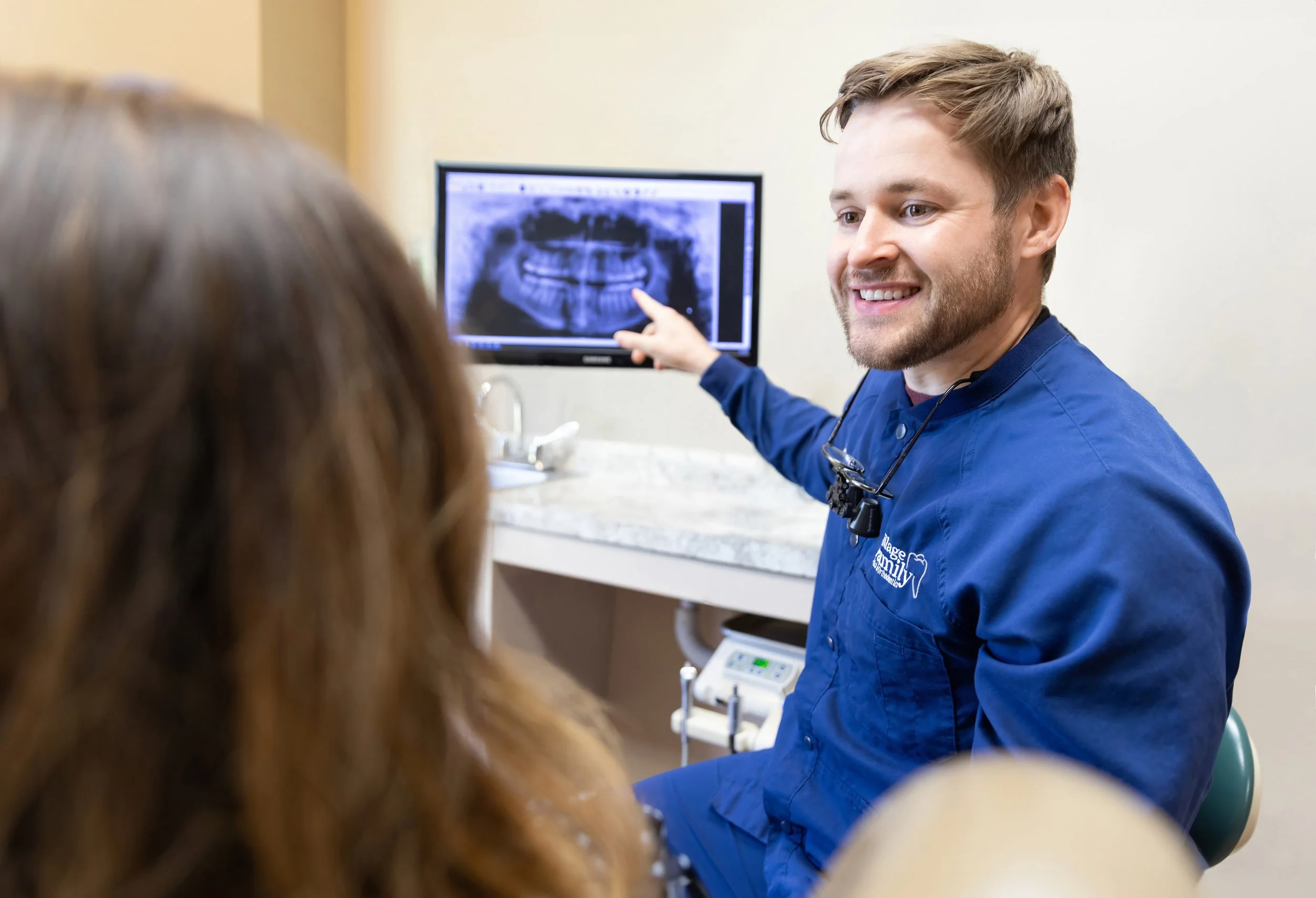 Dentist showing a patient a dental X-ray on a screen in a clinic.