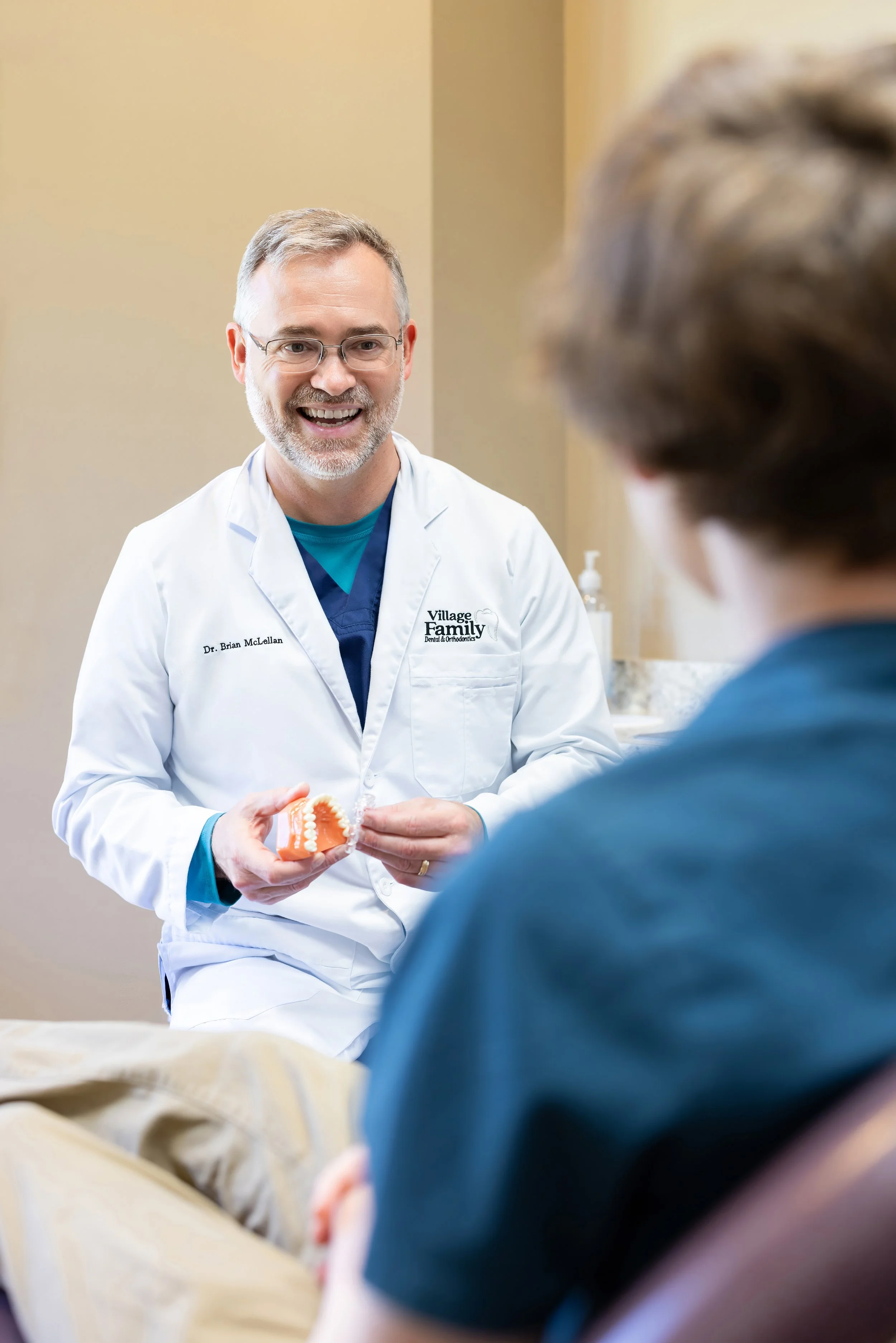 A dentist demonstrates dental prosthetic on a model to a patient in a consultation room.