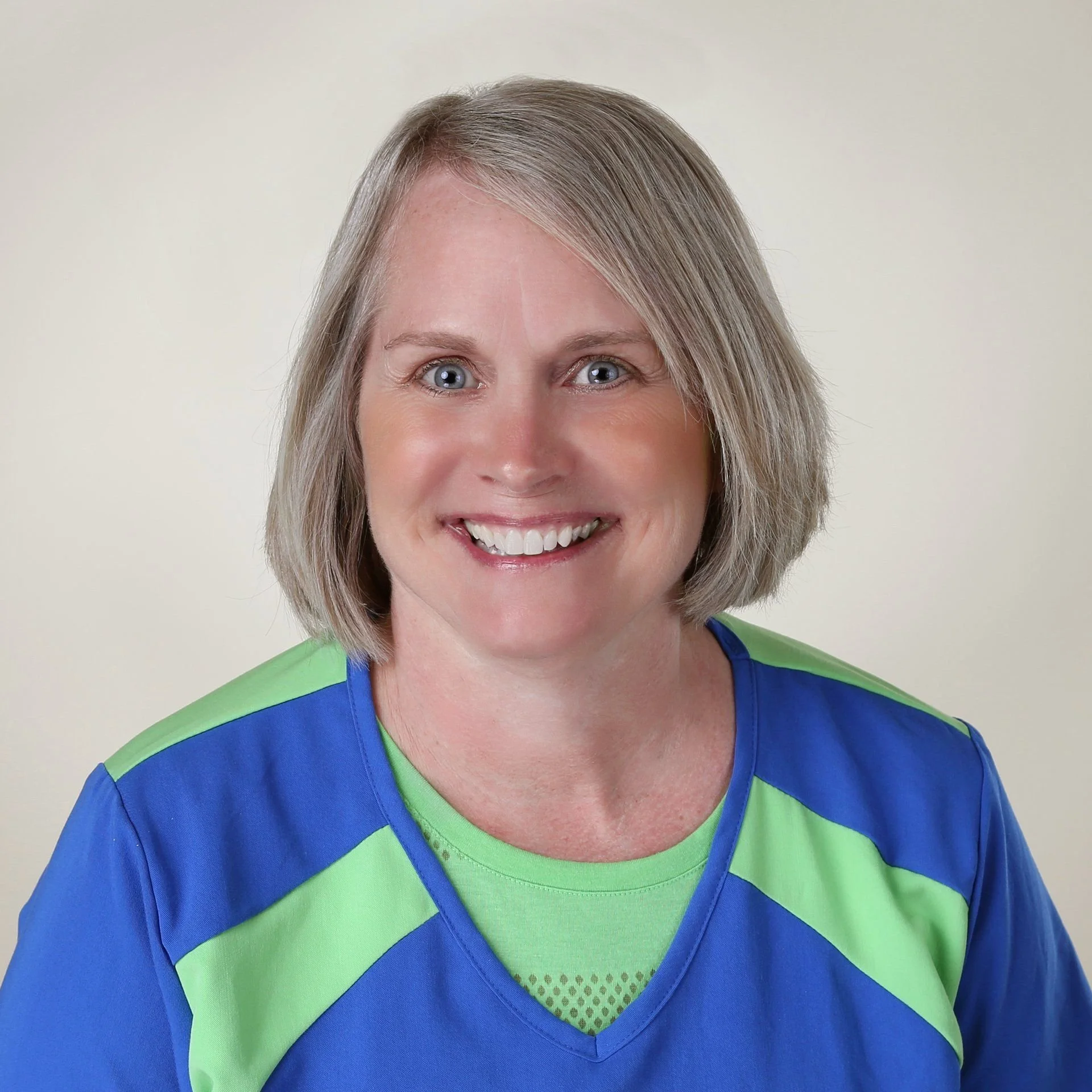 Portrait of a smiling woman with blonde hair, wearing a blue and green sports jersey, against a neutral background.