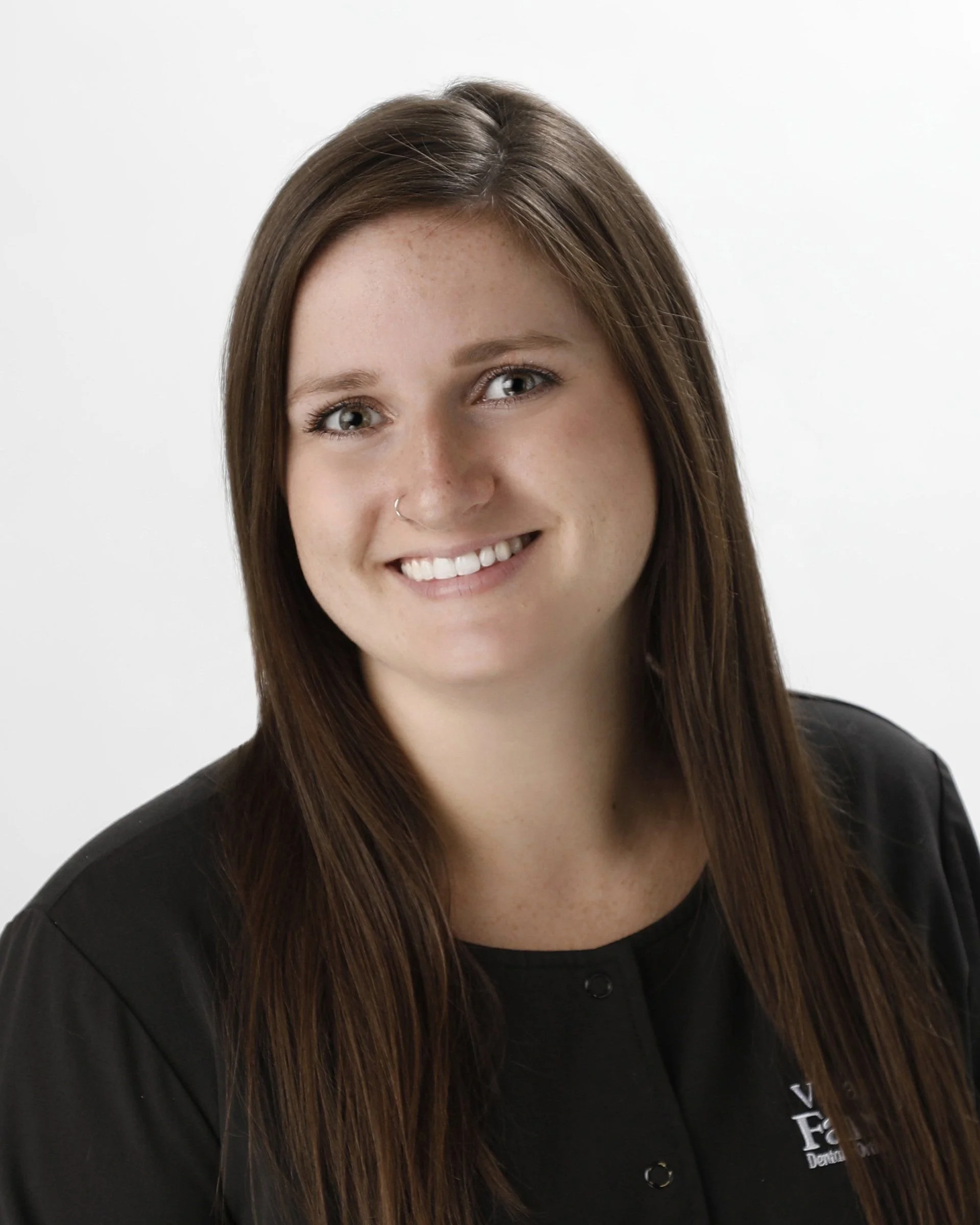 Portrait of a young woman with long brown hair, wearing a black shirt, smiling, against a white background.
