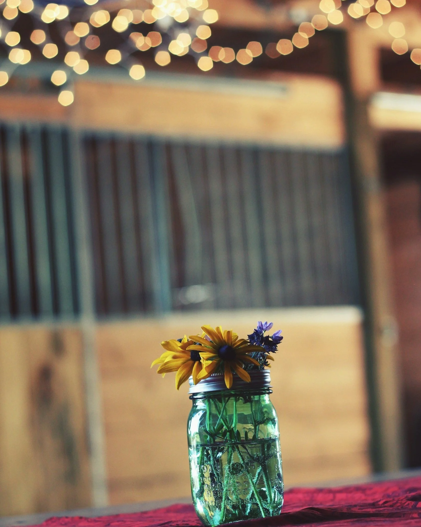 An image of a mason jar vase with flowers and twinkle lights in the distance.