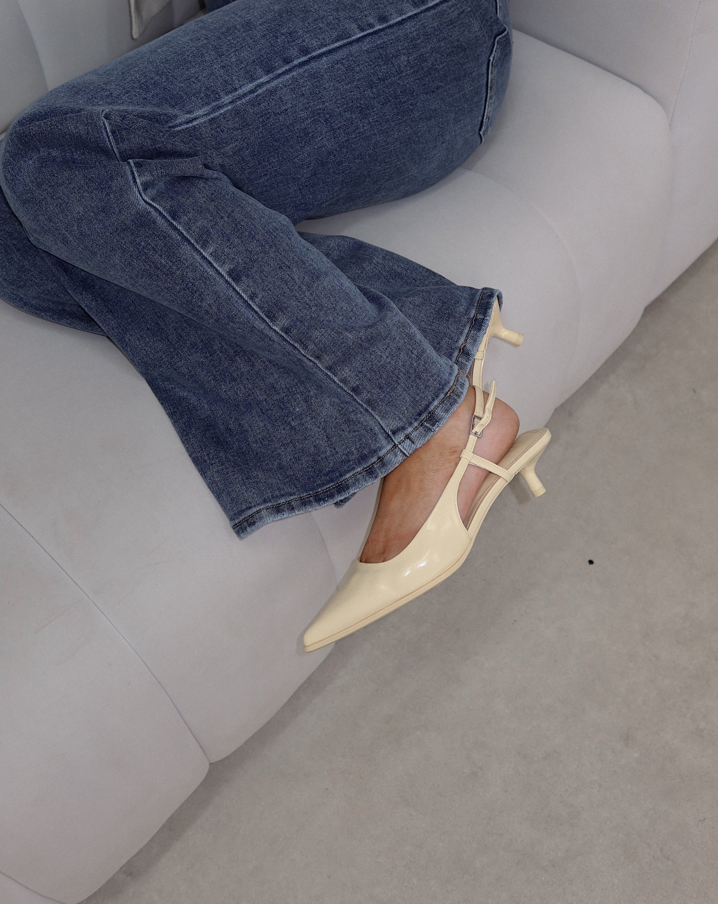 Person wearing blue jeans and cream-colored high-heeled shoes, sitting on a light gray sofa.