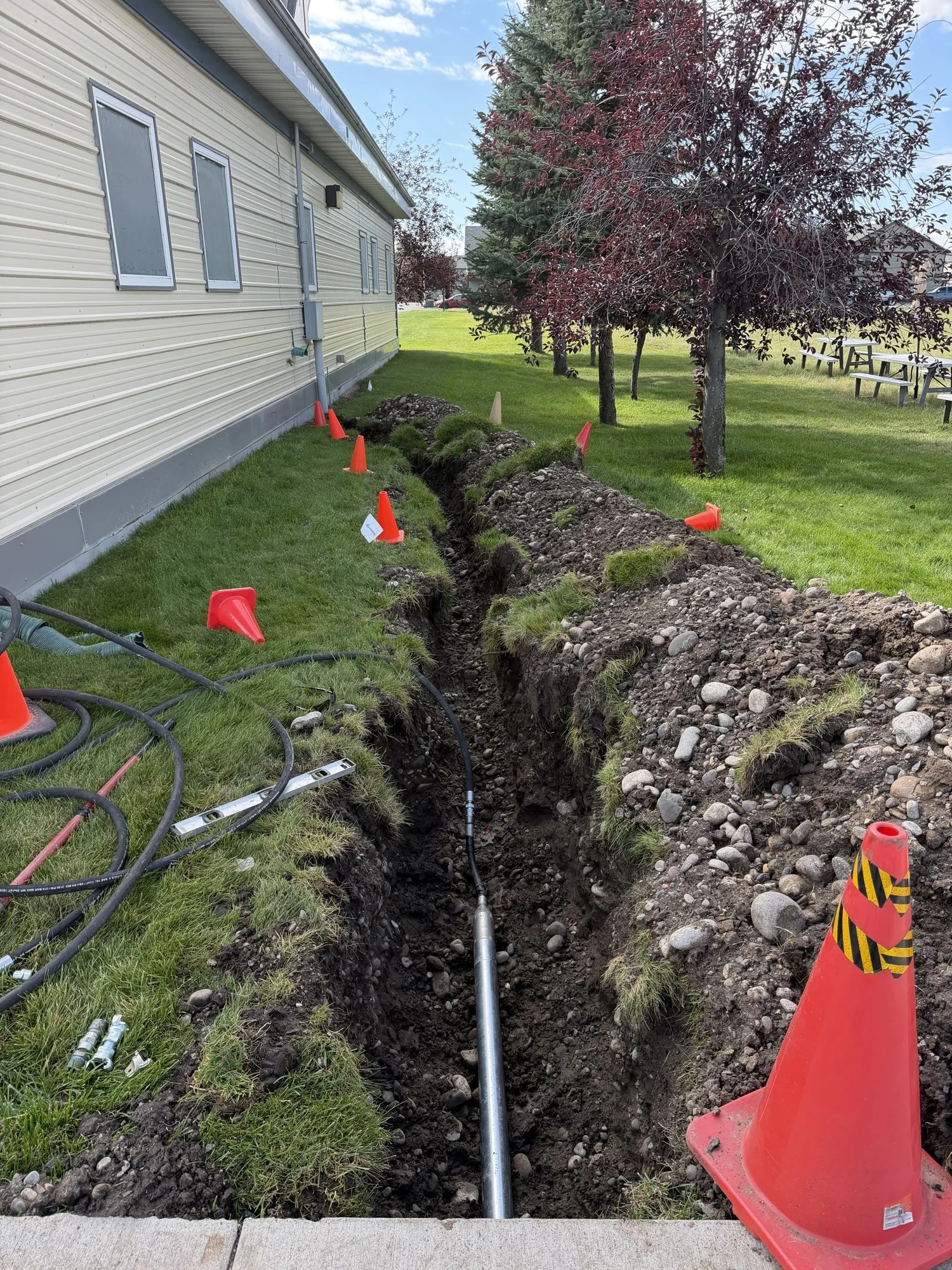 Open trench with conduit and marker flags along a campus building