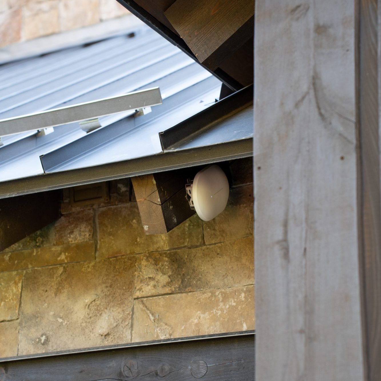 Outdoor WiFi access point mounted under a timber eave on a stone mountain home, installed by Big Sky Wired