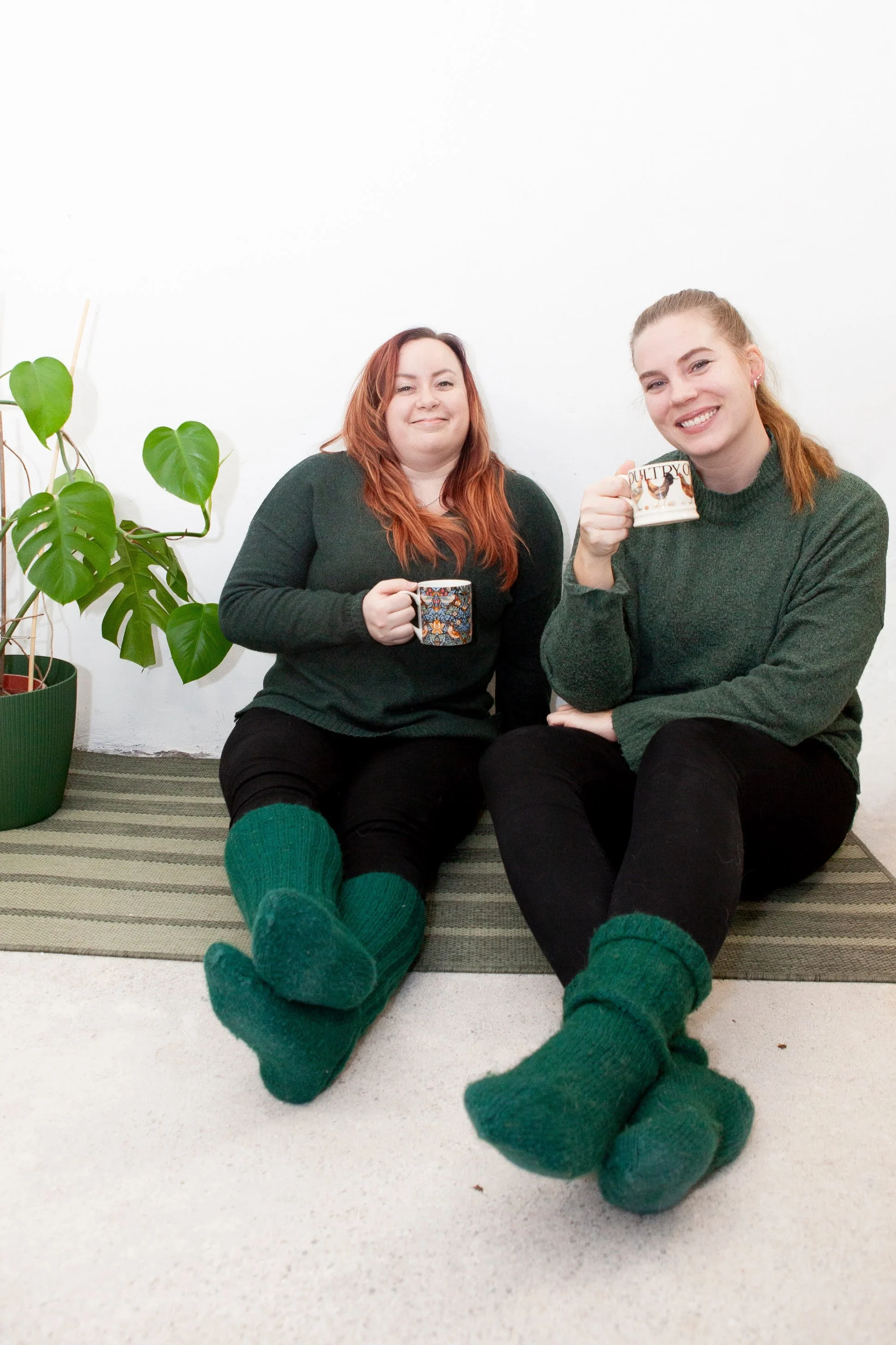 Kaksi kirjanpitäjää istuu matolla, juoden kupit kahvia ja hymyillen.