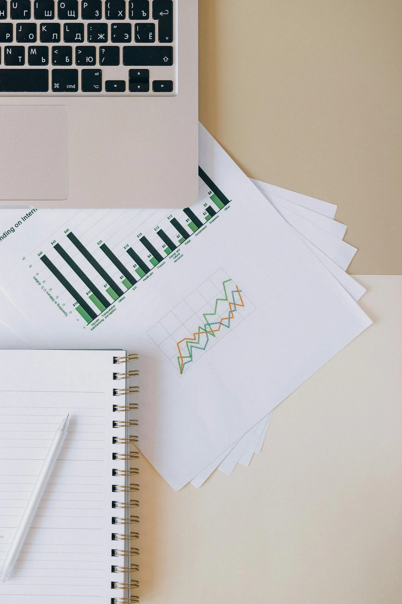 Tietokone ja papereita, joissa on grafiikoita sekä muistiinpanovihko ja pyyhekumi